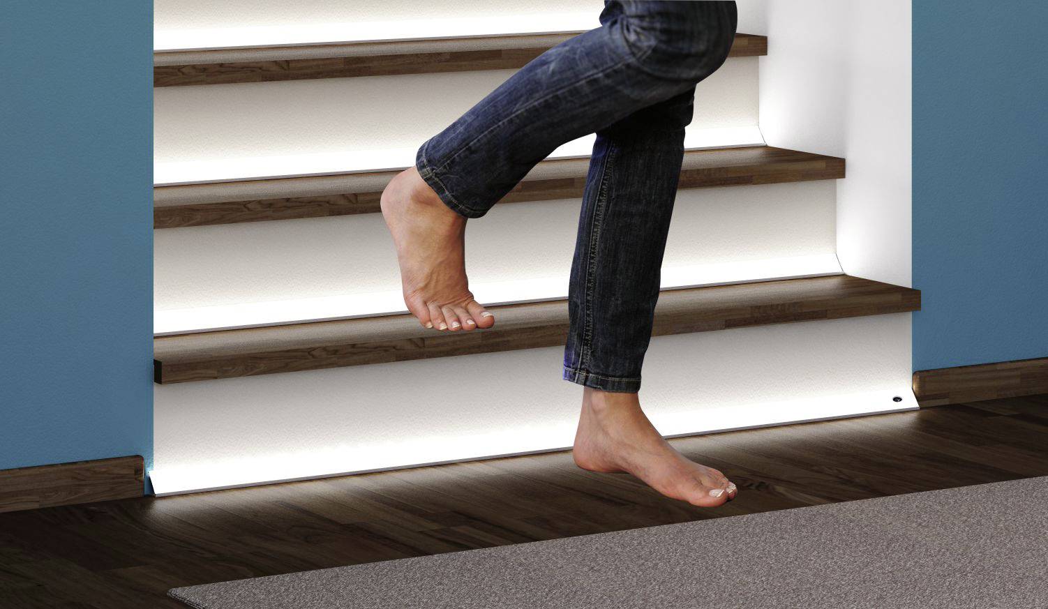 Osoba idzie boso po schodach we wnętrzu o nowoczesnym wystroju. Stopnie schodów są podświetlone światłem pośrednim.