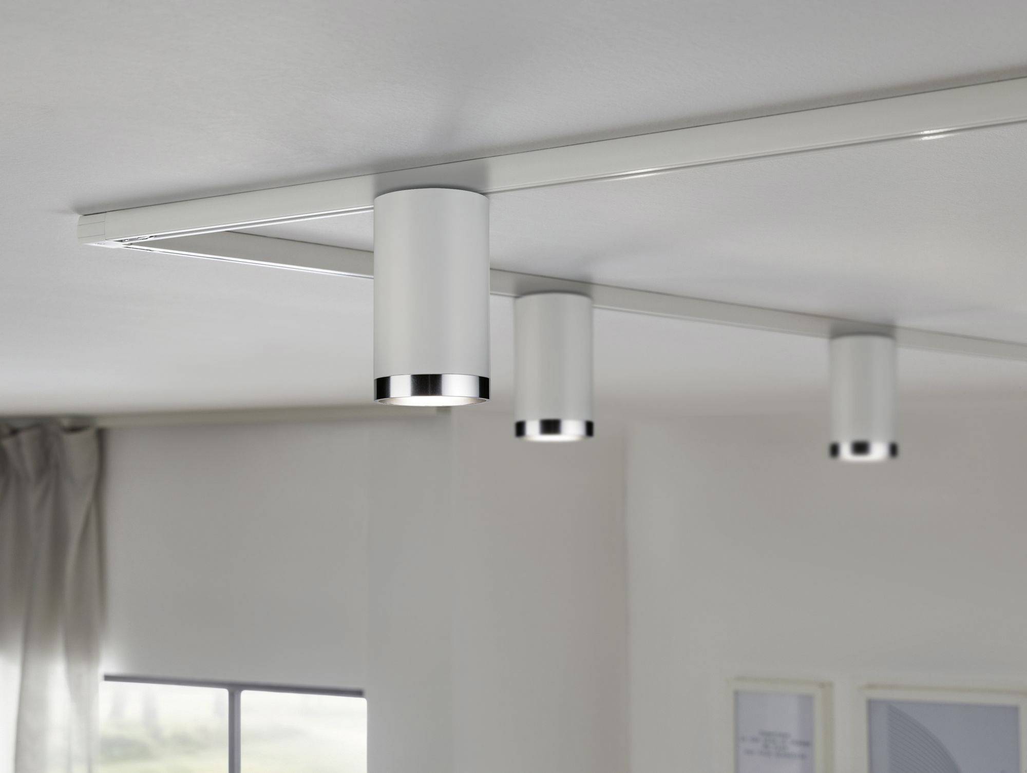 Trzy cylindryczne lampy sufitowe zamontowane równomiernie wzdłuż szyny oświetlają pomieszczenie w subtelny sposób.