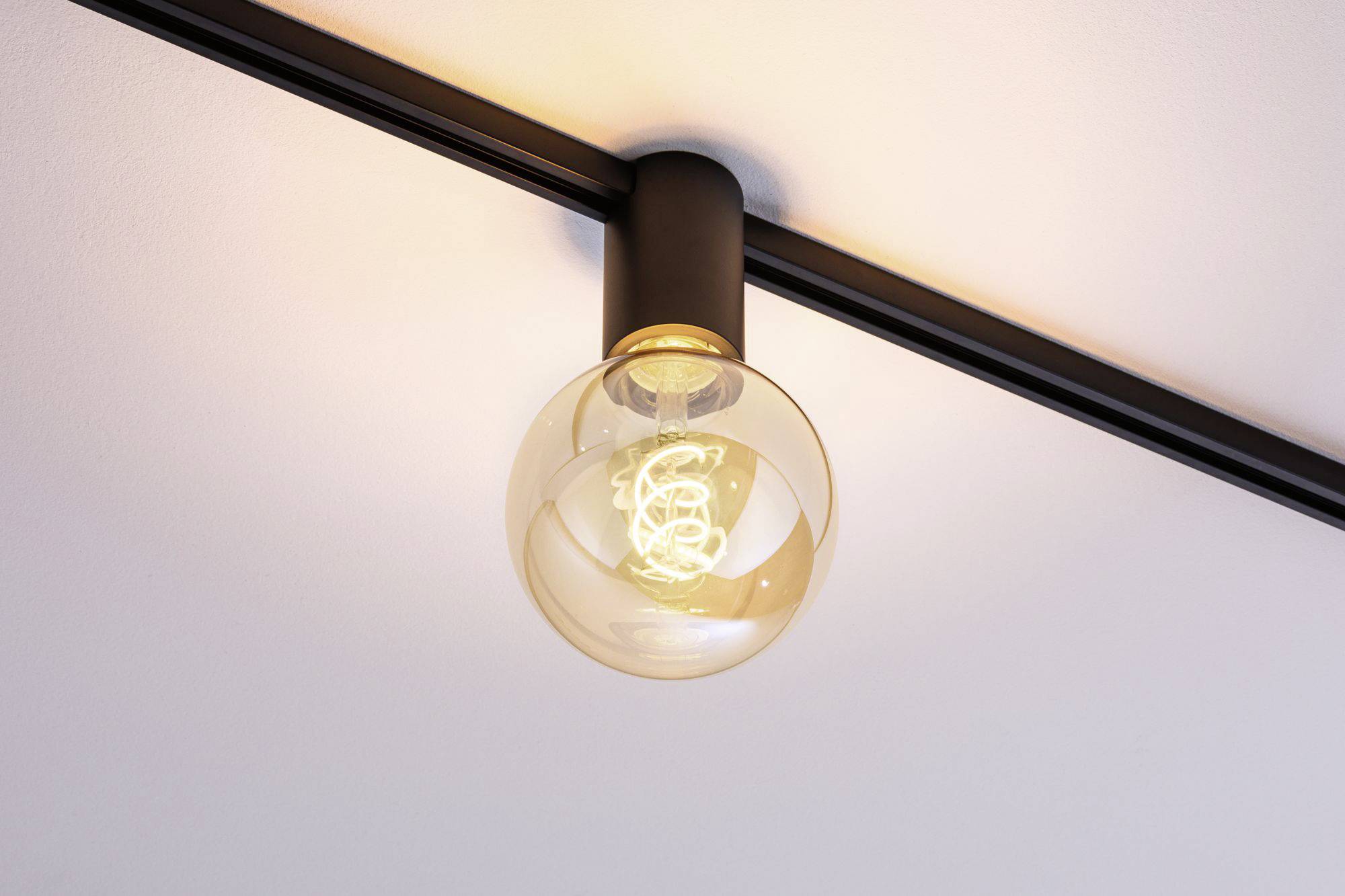 Nowoczesna lampa sufitowa z okrągłą szklaną osłoną i widoczną żarówką świeci w pomieszczeniu.