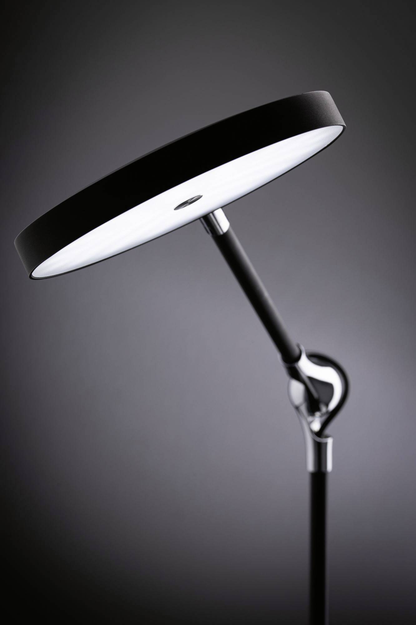 Lampa stojąca z okrągłym białym abażurem i czarną podstawą, w stylistyce nowoczesnego designu, przedstawiona w minimalistycznie oświetlonym pomieszczeniu.
