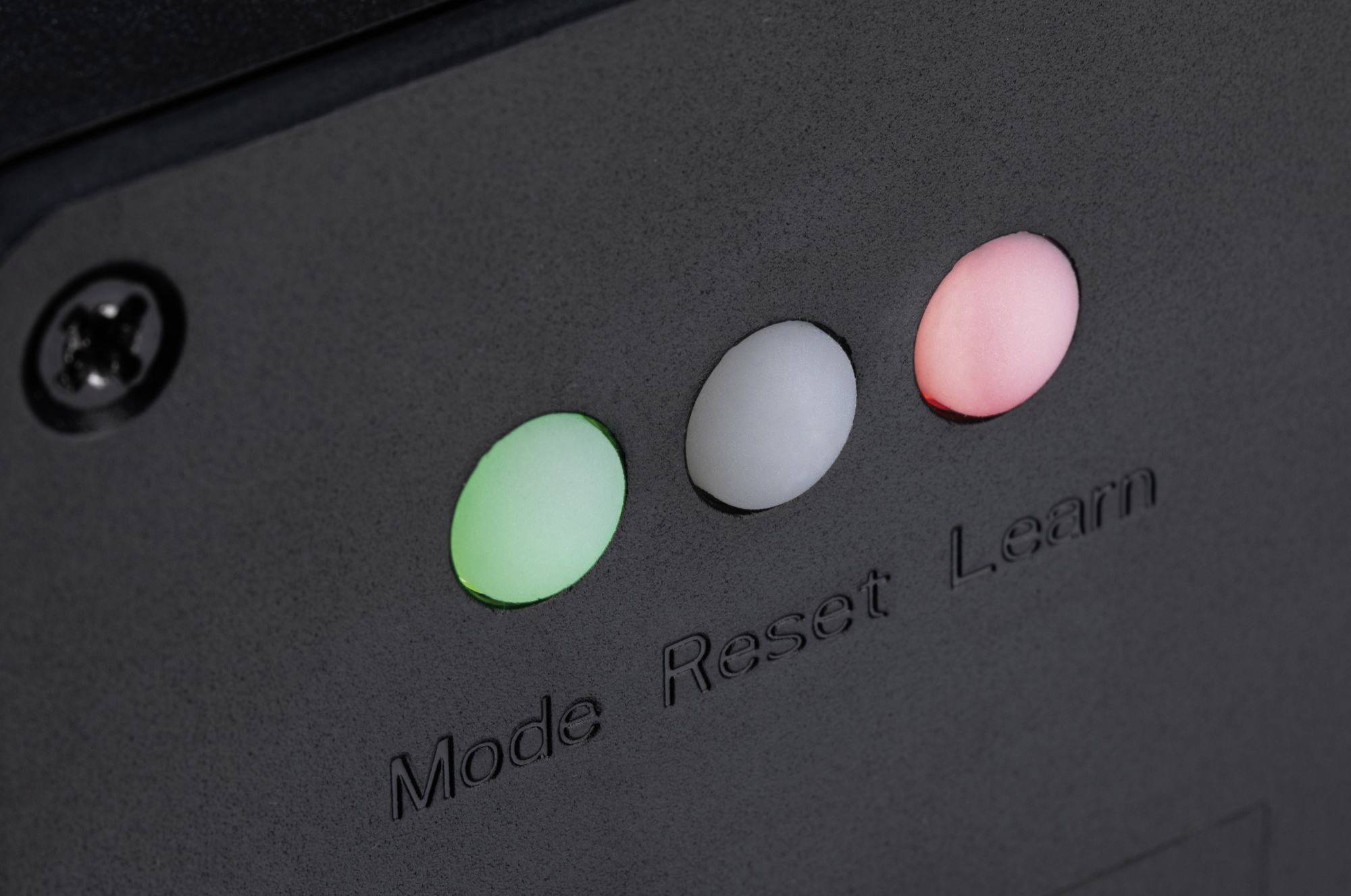 Trzy przyciski na urządzeniu: 'Tryb' (zielony), 'Reset' (biały), 'Uczenie' (czerwony). Są rozmieszczone na czarnej powierzchni.