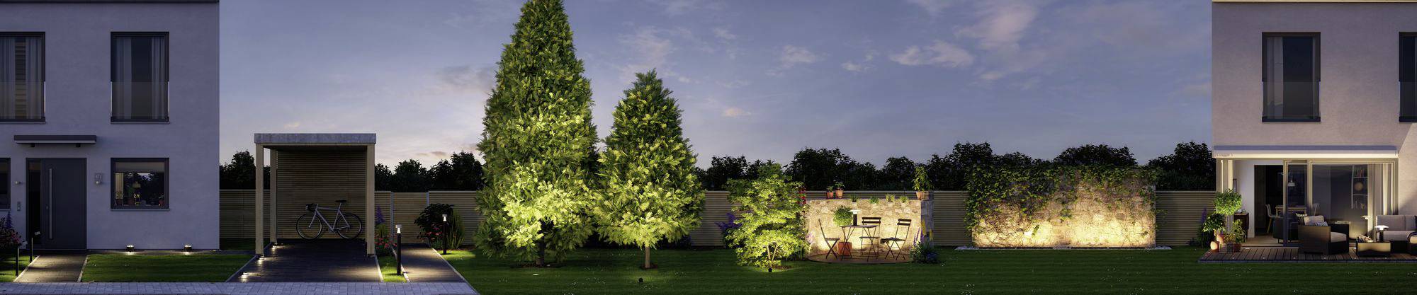 Ogród wieczorową porą, otoczony drzewami i krzewami, z nowoczesnymi domami w tle. Oświetlenie podkreśla rośliny i tworzy przytulną atmosferę.
