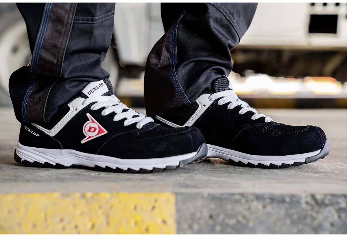 Para czarnych butów sportowych z białą podeszwą i czerwonym logo jest noszona przez osobę stojącą na betonowym bloku.