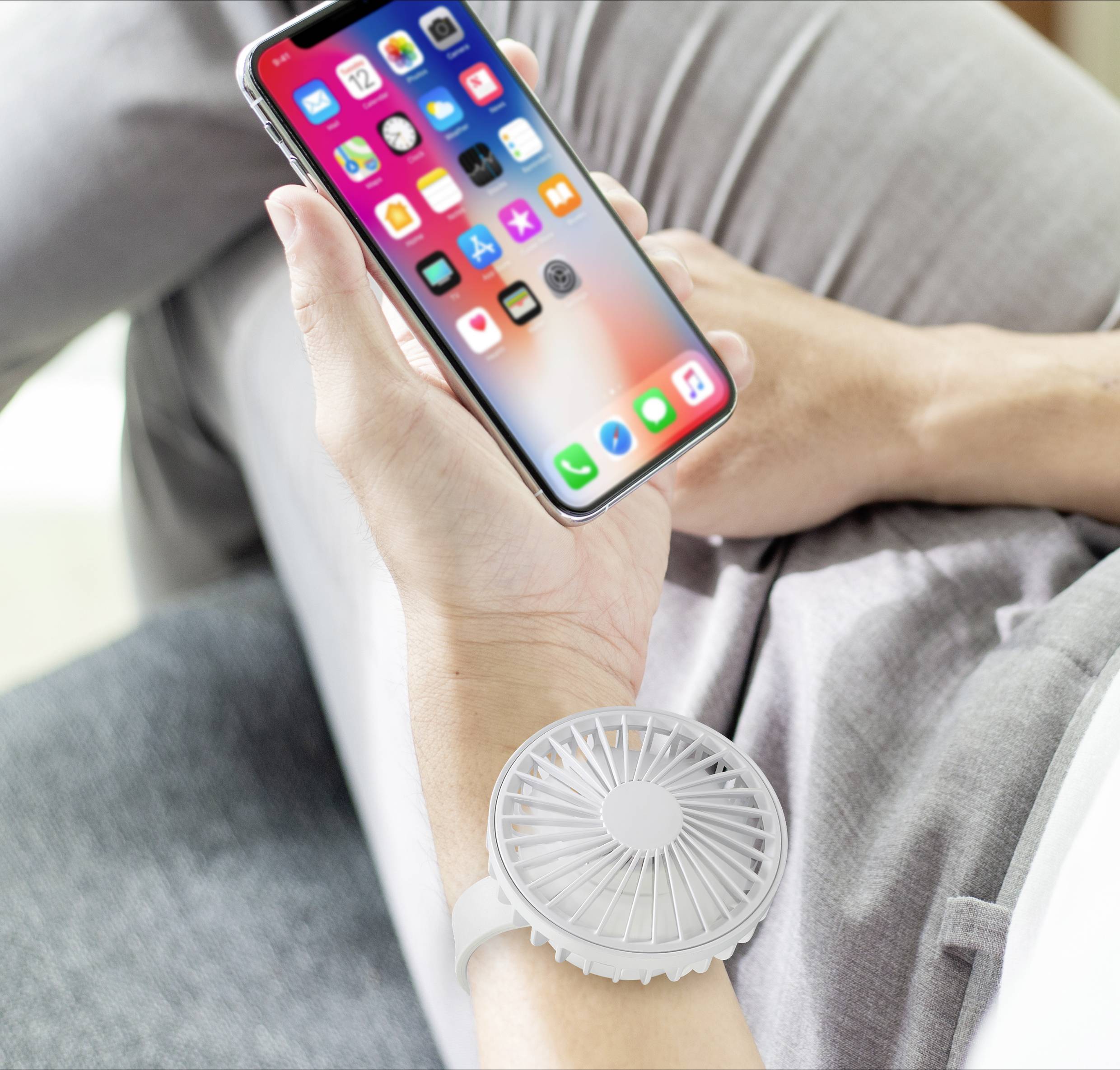 Osoba trzyma smartfon w ręku, podczas gdy mały wentylator jest przymocowany do nadgarstka.