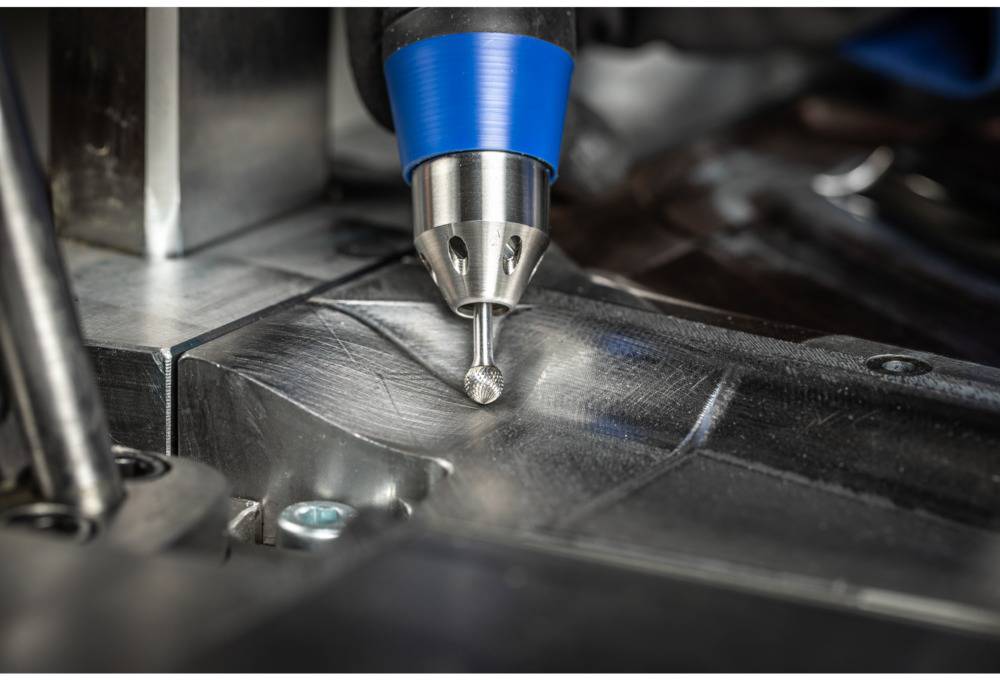 Przemysłowe frezowanie CNC precyzyjnie obrabia powierzchnię metalową. Zbliżenie na głowicę frezującą z niebieskim uchwytem.