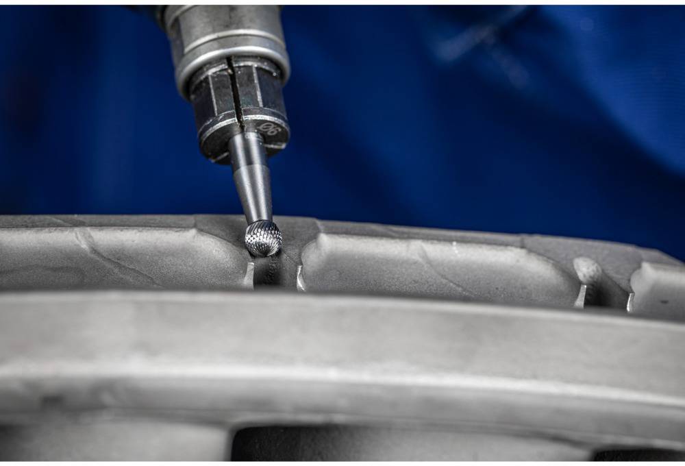 Zbliżenie metalowego narzędzia obrabiającego skomplikowaną powierzchnię metalowego elementu na rozmytym tle.