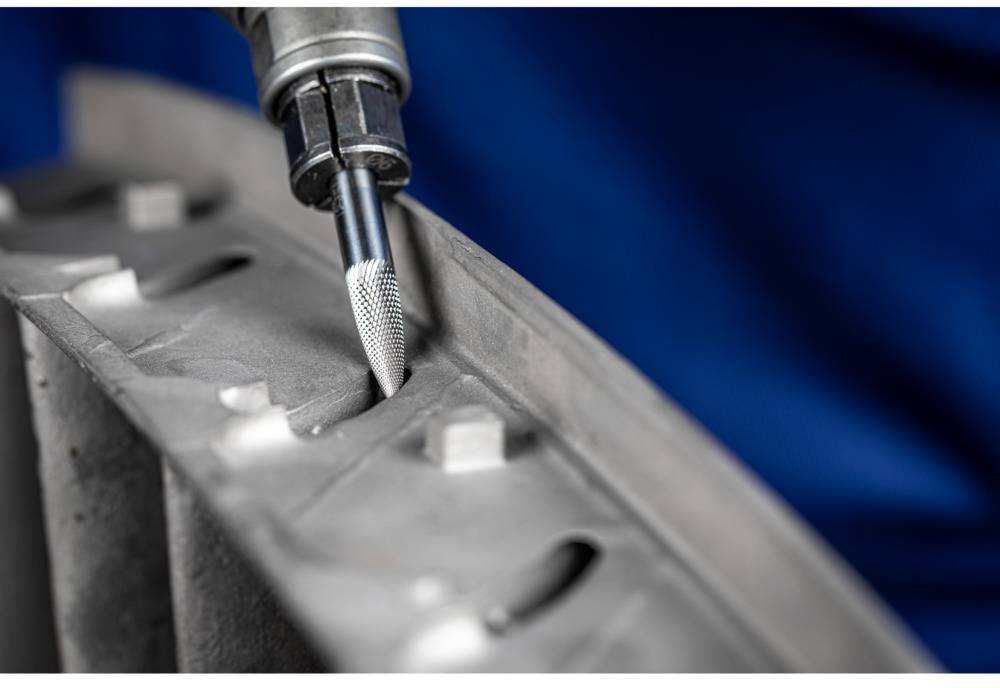 Zbliżenie wiertła obrabiającego metalową powierzchnię. Tło jest rozmyte w odcieniach niebieskiego. Ostrość skierowana jest na precyzyjną pracę.