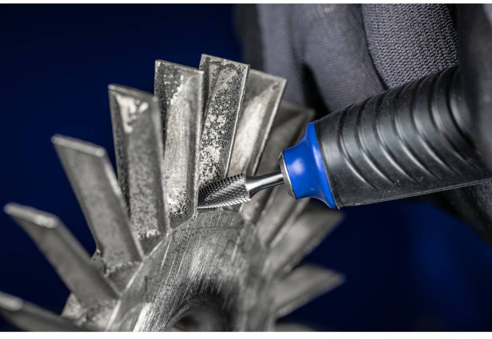 Dłoń trzyma obracające się narzędzie używane do szlifowania lub polerowania metalowego elementu. Tło jest rozmyte.