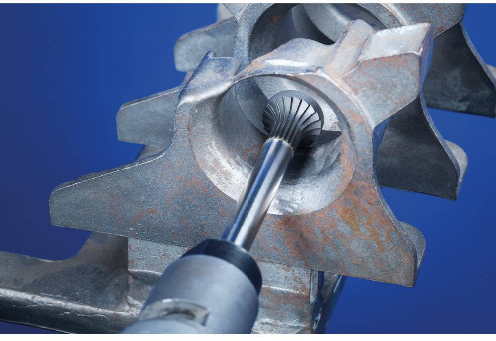 Metalowe narzędzie poleruje dużą okrągłą formę metalową na niebieskim tle. Widoczne są ślady rdzy.