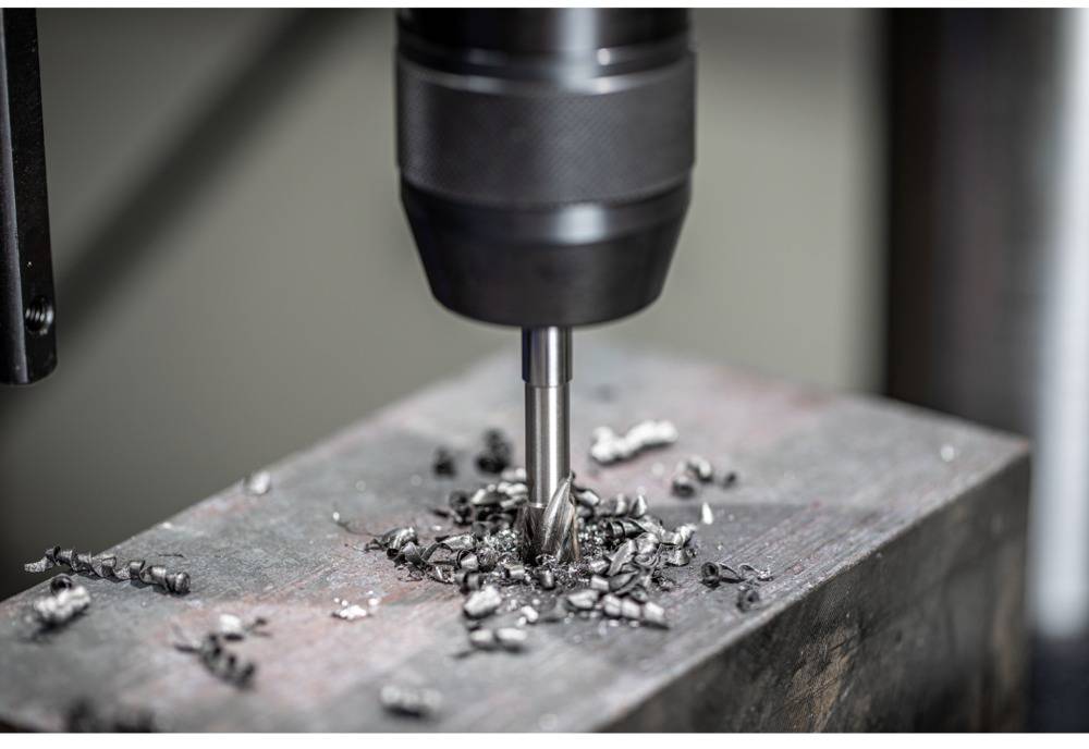 Wiertło metalowe wierci w kawałku metalu. Wióry leżą wokół miejsca wiercenia.