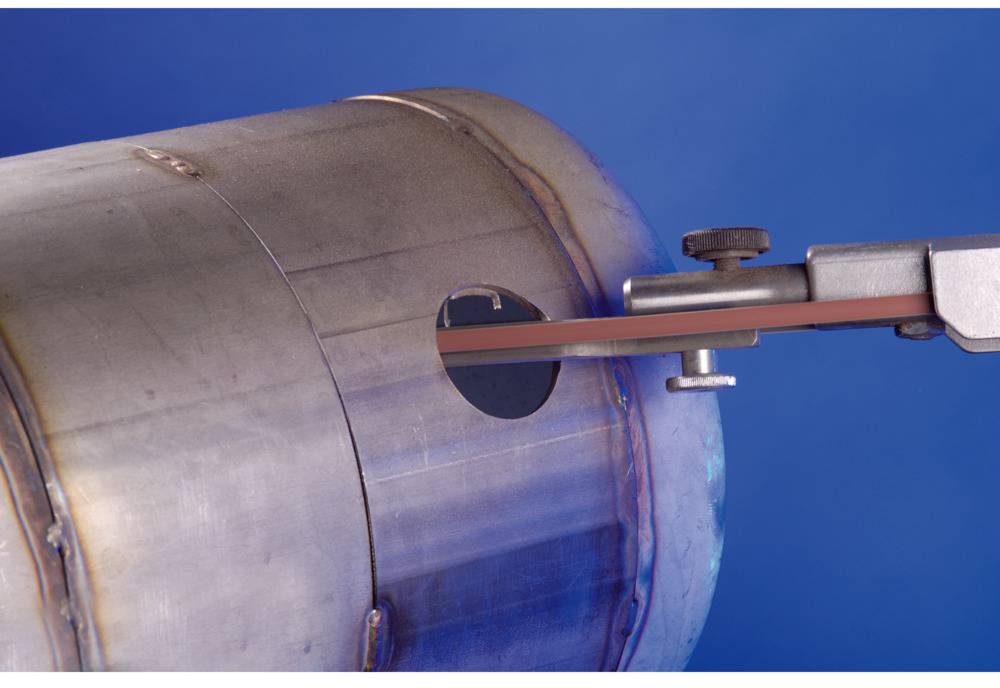 Metalowy cylinder z wystającym narzędziem włożonym w okrągły otwór na niebieskim tle.