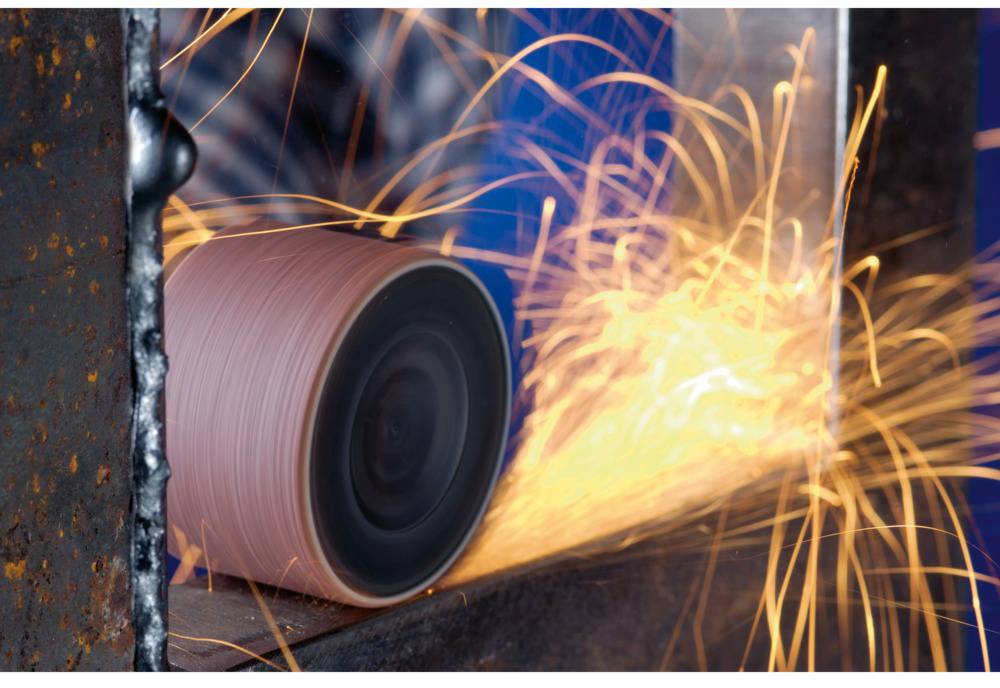 Maszyna szlifuje metal, podczas gdy lecą iskry. Obracająca się tarcza szlifierska obrabia krawędź metalu.