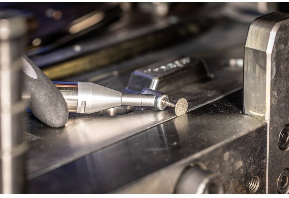 Zbliżenie kątnicy na metalowej powierzchni, z małą tarczą szlifierską na końcu.