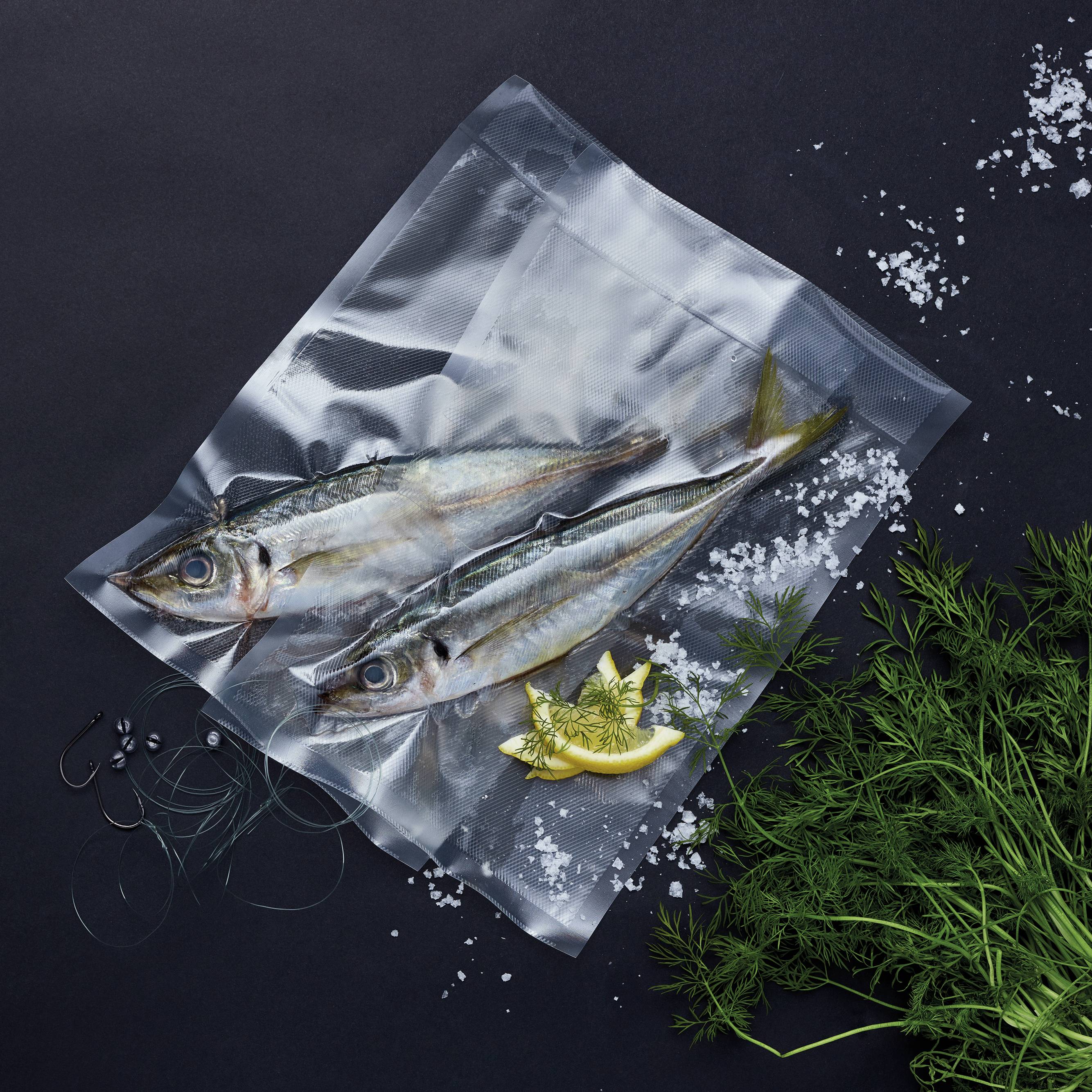 Trzy świeże ryby w opakowaniu próżniowym z plasterkami cytryny i koperkiem, ozdobione solą na czarnym tle.