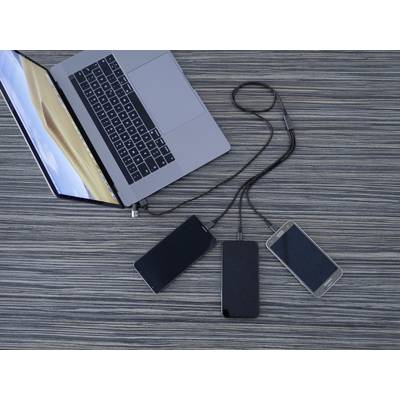 Laptop jest podłączony przewodami do dwóch powerbanków i smartfona, leżąc na stole z widocznym słojem drewna.