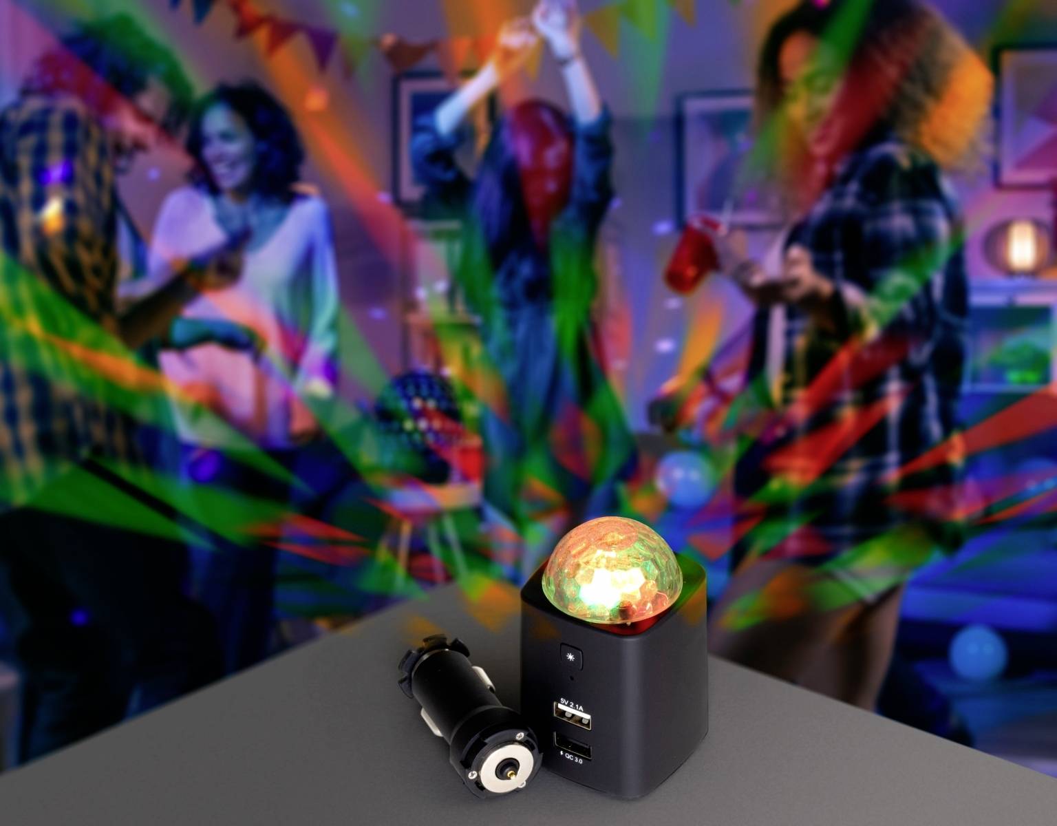 Kolorowa scena imprezy z czterema osobami tańczącymi. Na pierwszym planie stoi świecąca lampa z podłączonym przewodem USB, umieszczona na stole.