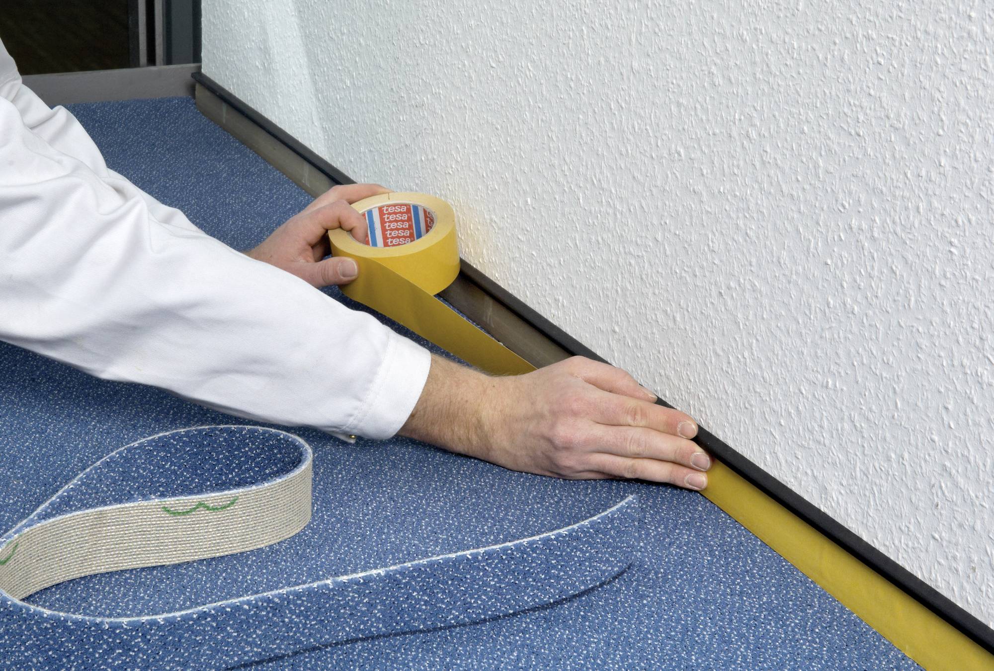 Osoba przykleja żółtą taśmę klejącą do ściany w pobliżu podłogi dywanowej, aby zapewnić czysty malowanie lub ochronę.