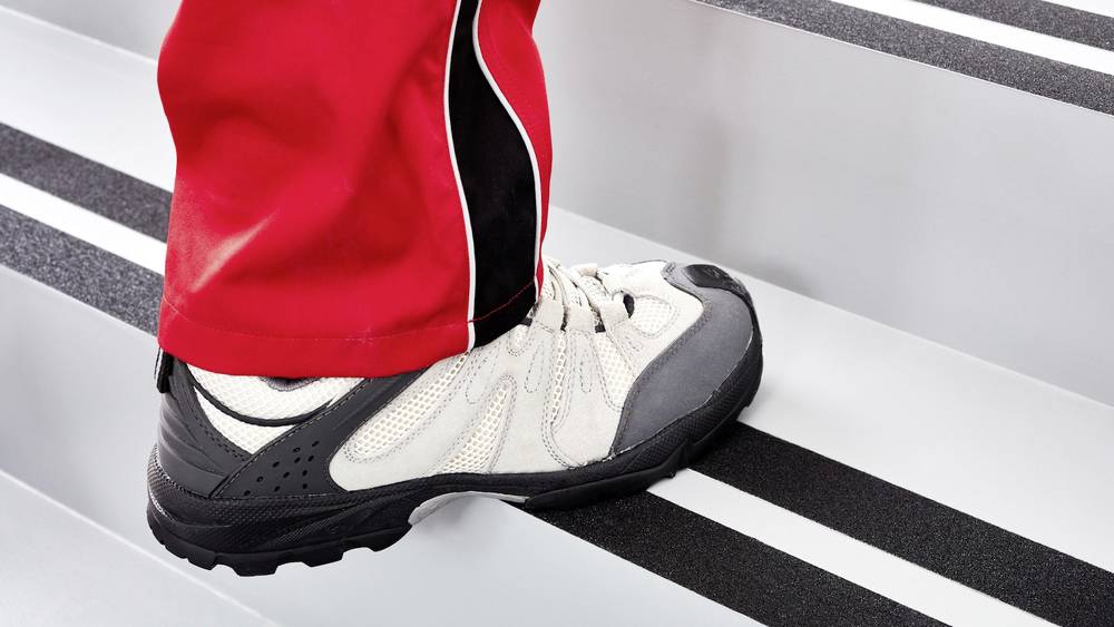 Osoba w czerwonych spodniach wspina się po schodach. Fokus na białym bucie sportowym.