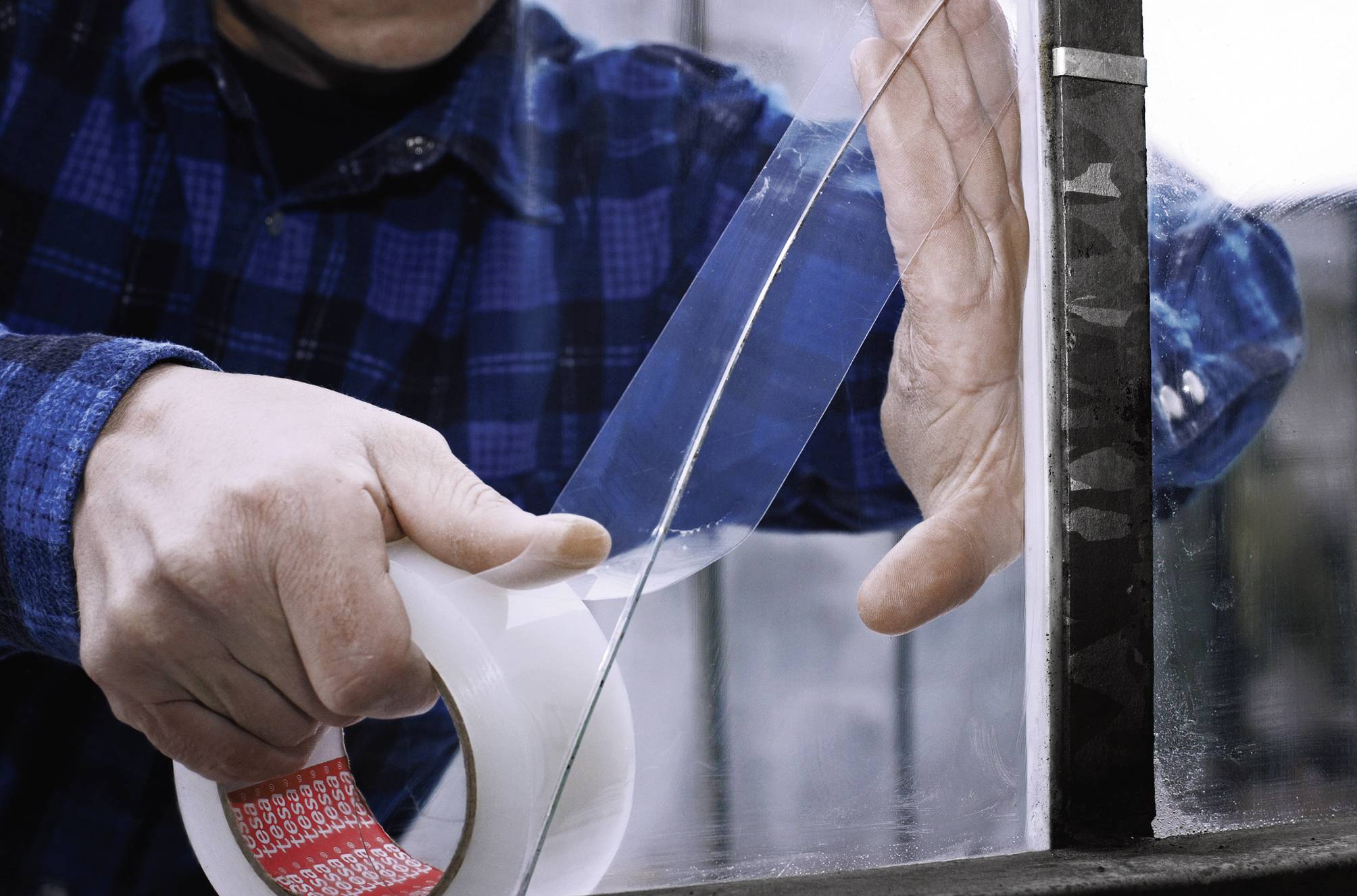 Osoba mocuje przezroczystą taśmę klejącą na szybie, prawdopodobnie w celach naprawczych lub izolacyjnych.