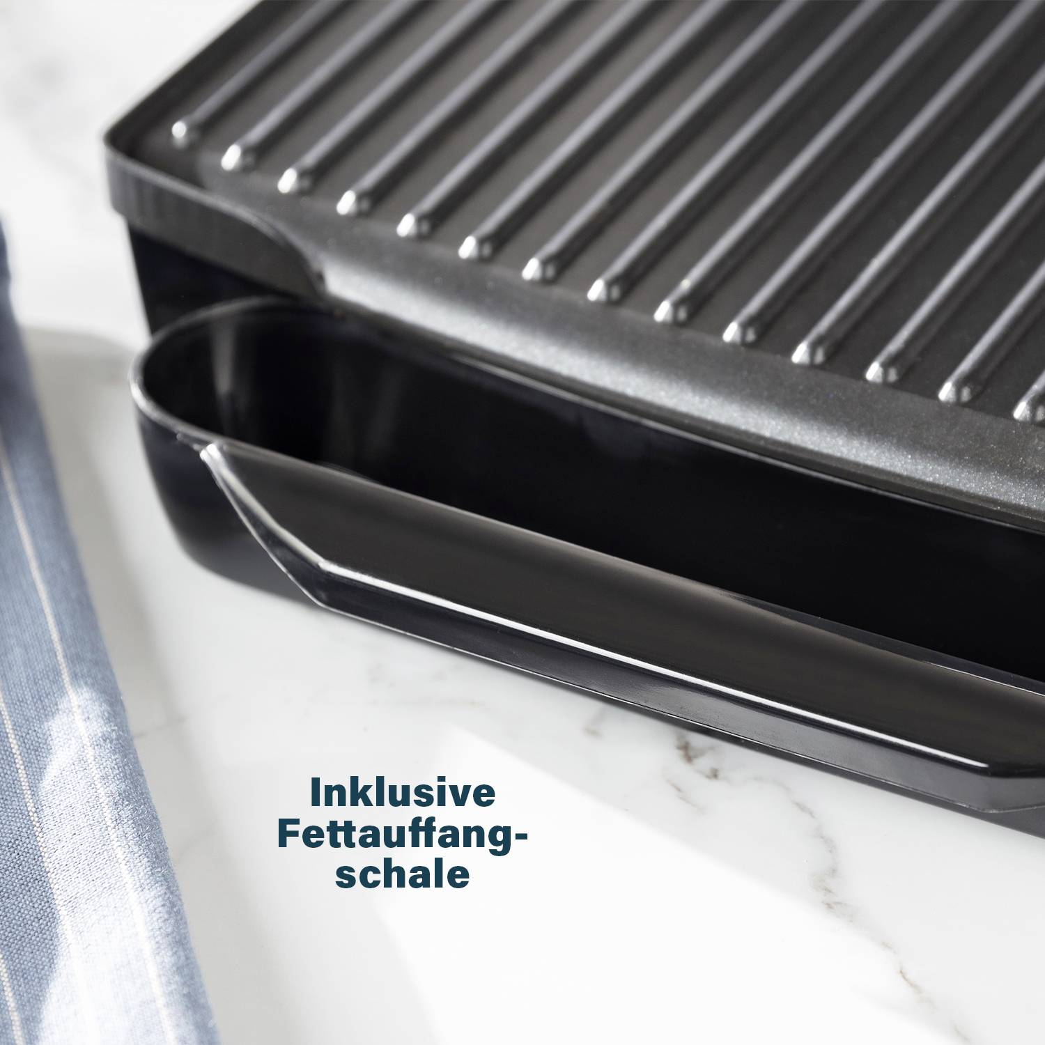 Taca do zbierania tłuszczu w grillu, przeznaczona do gromadzenia nadmiaru tłuszczu podczas grillowania. Obok widać niebieską szmatkę.