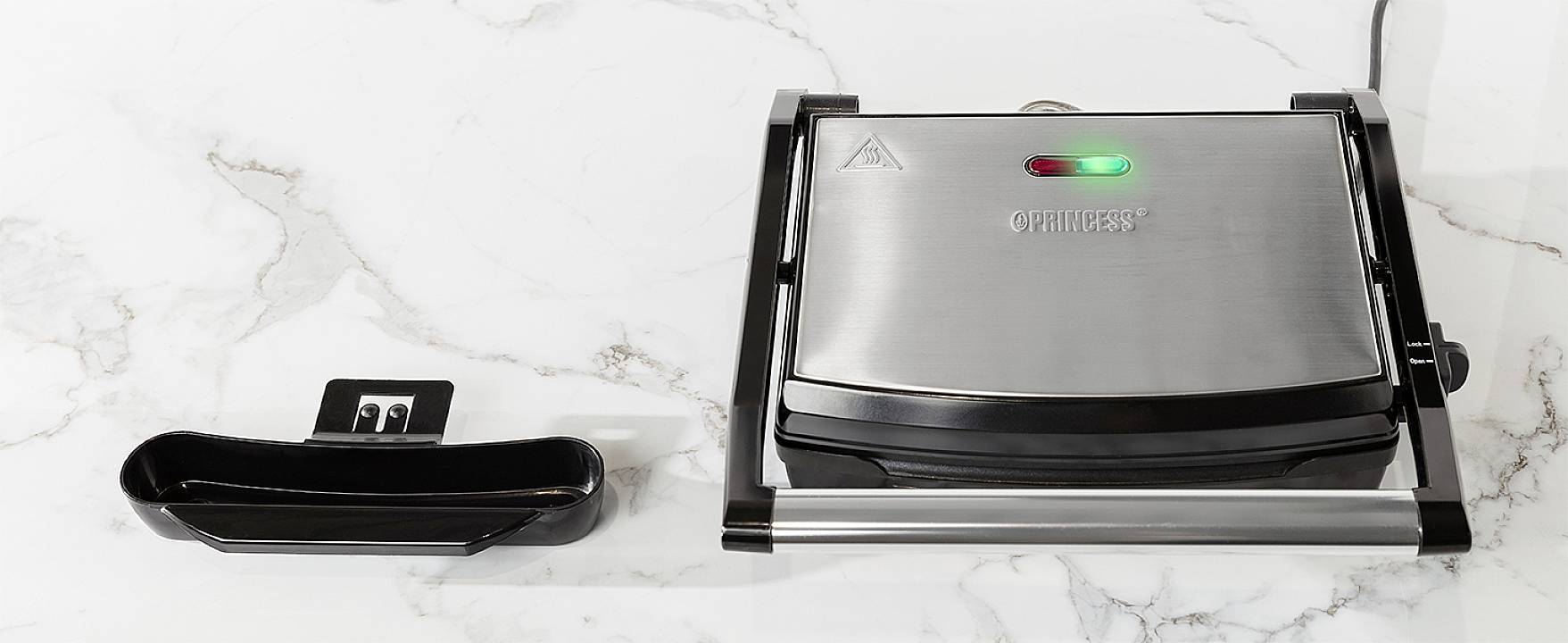 Elektryczny grill na marmurowym blacie z zamkniętą pokrywą. Obok znajduje się taca ociekowa.