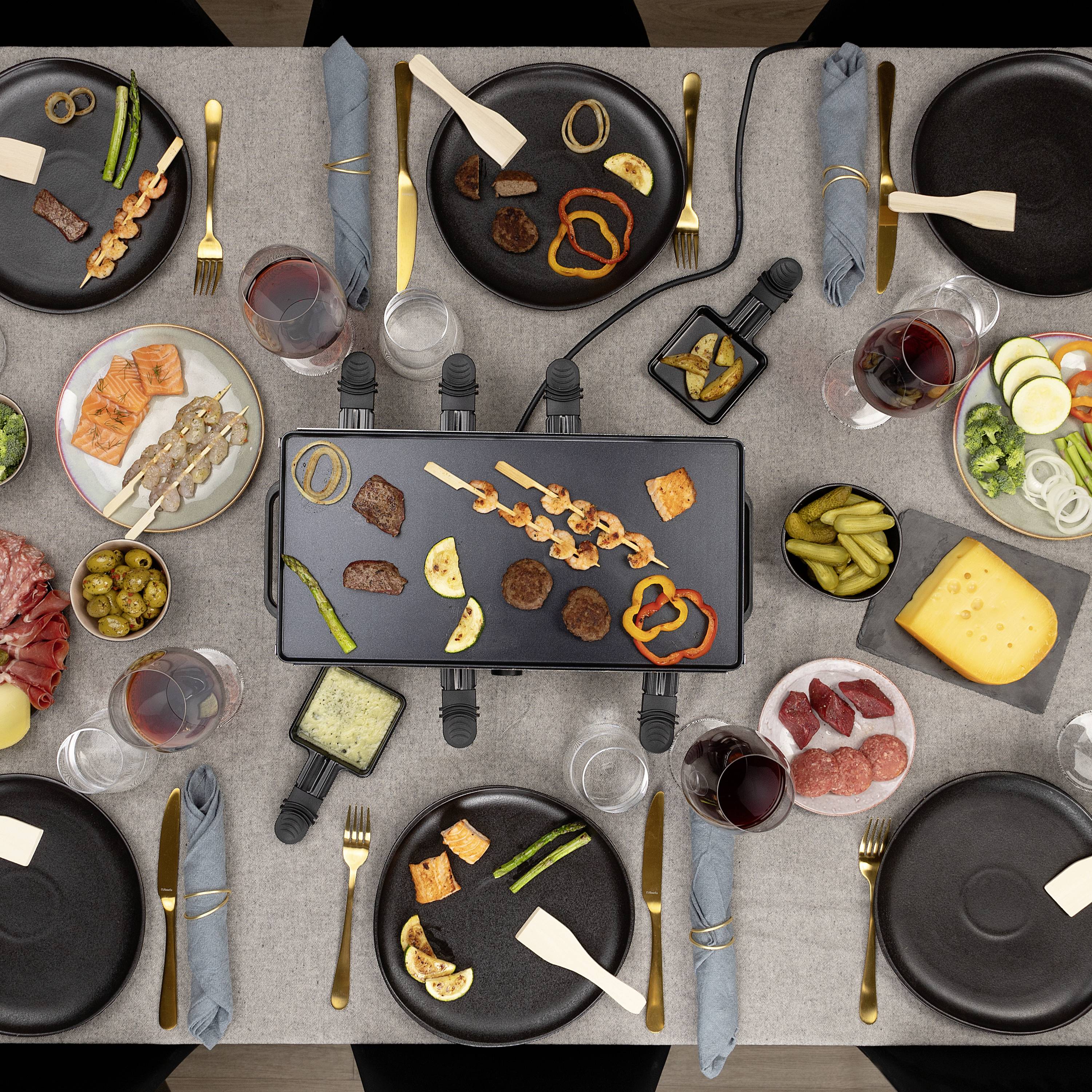 Nakryty stół z grillem raclette pośrodku, otoczony talerzami z warzywami, mięsem, serem, plastrami chleba i kieliszkami do wina.