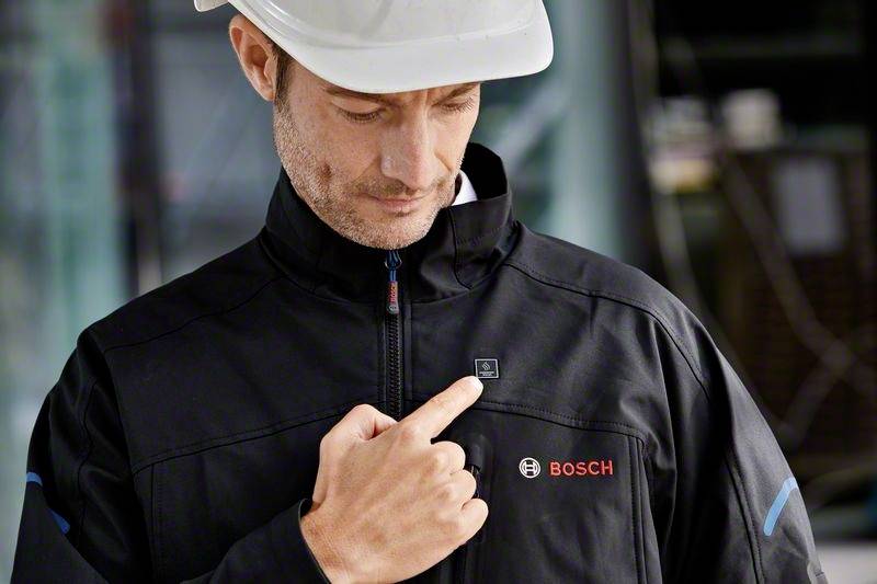 Pracownik w kasku ochronnym wskazuje na elektroniczny moduł na kurtce z logo 'BOSCH'. Kontekst: prezentacja produktu.
