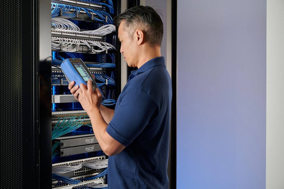 Technik w serwerowni sprawdza za pomocą tabletu łączność kabli sieciowych w szafie serwerowej.