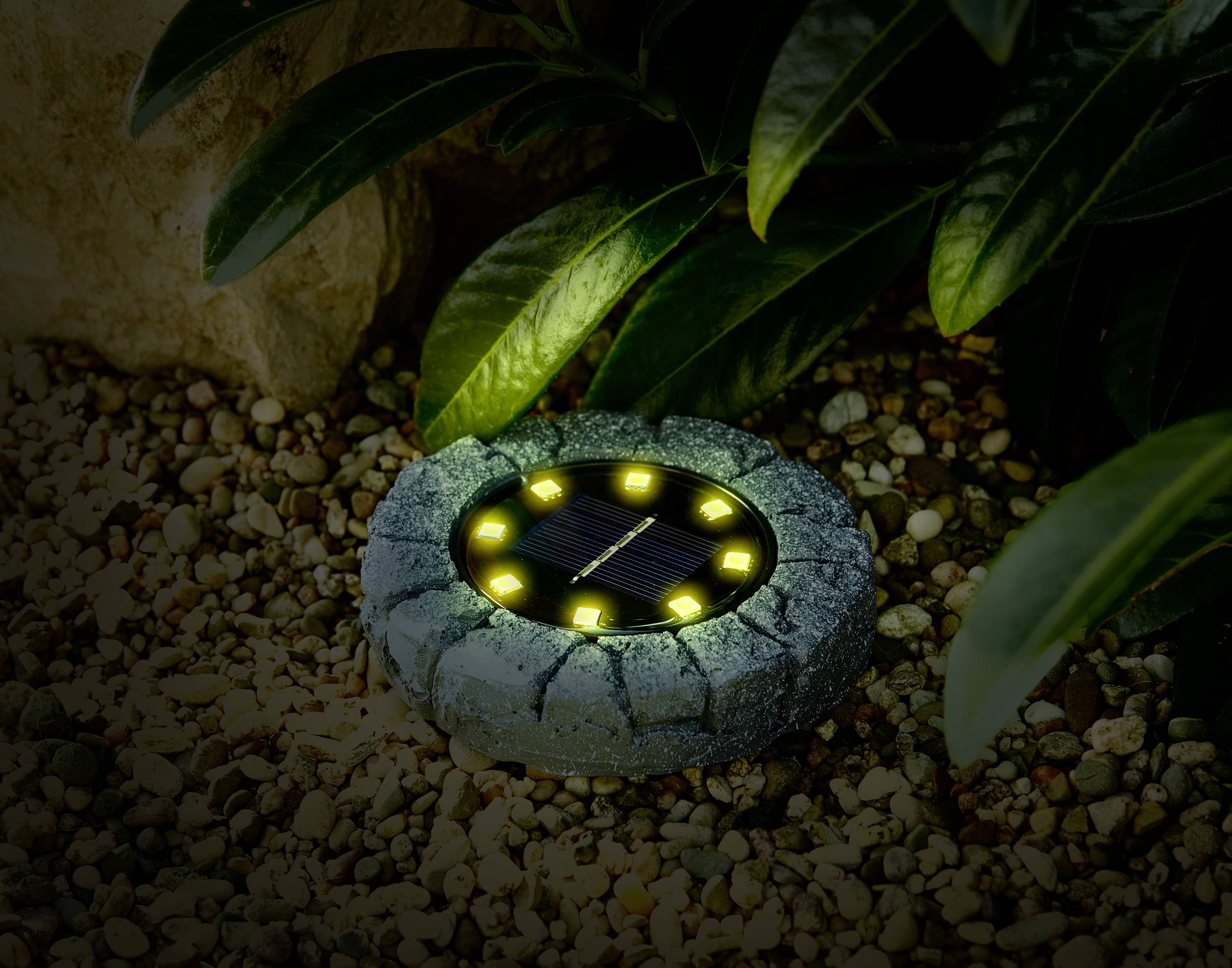 Solarne kamienne światło świeci w ogrodzie, otoczone żwirem i roślinami.