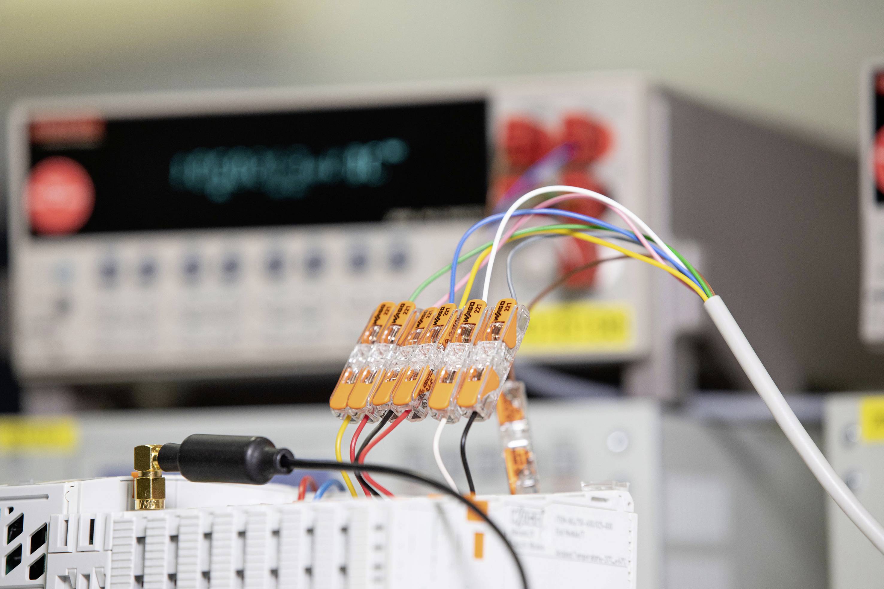 Laboratorium z elektrycznymi przyrządami pomiarowymi w tle. Na pierwszym planie przewody są połączone pomarańczowymi zaciskami.