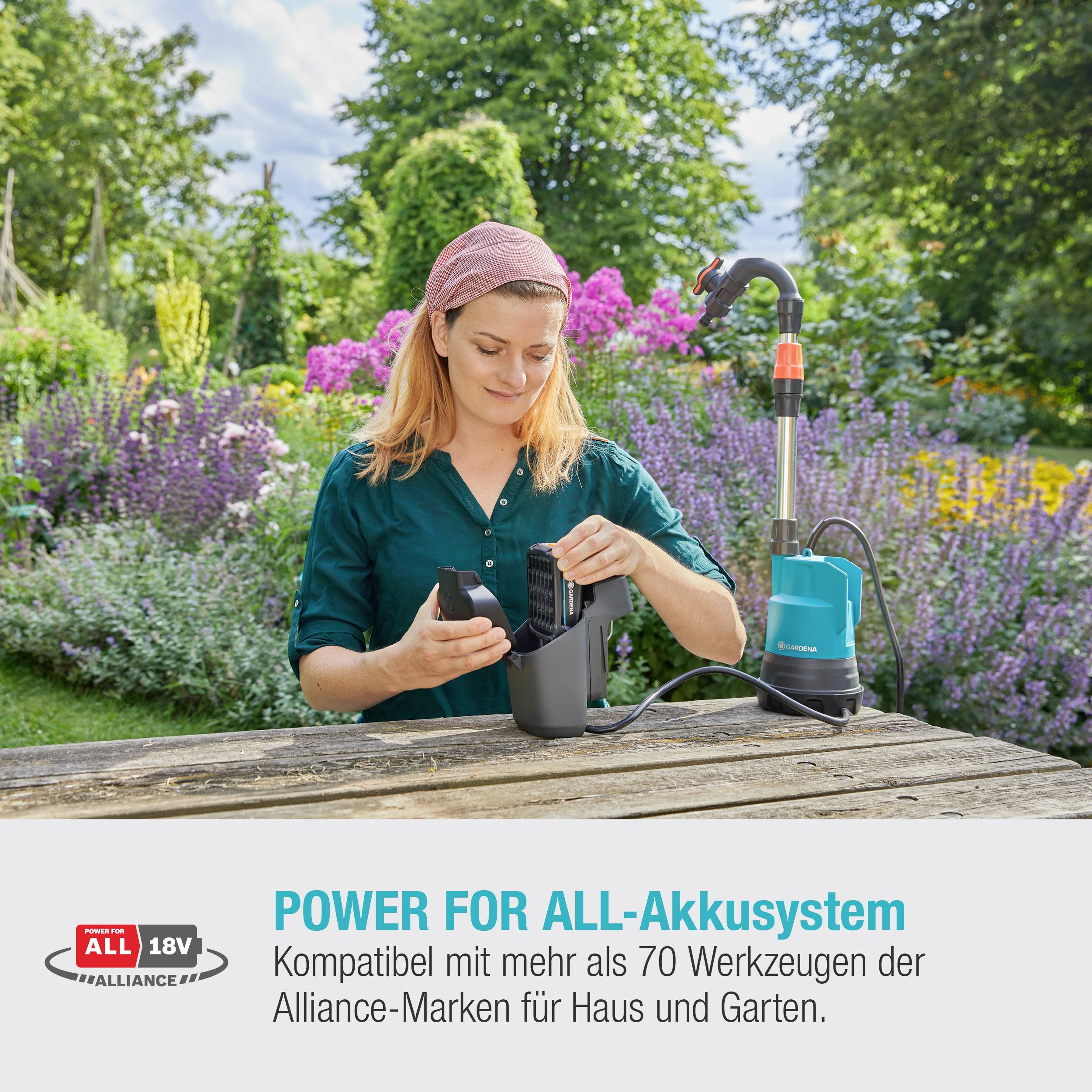 Osoba ładuje baterię ładowarką na zewnątrz. W tle widoczne są kolorowe kwiaty. Tekst: 'System akumulatorów Power for All'.