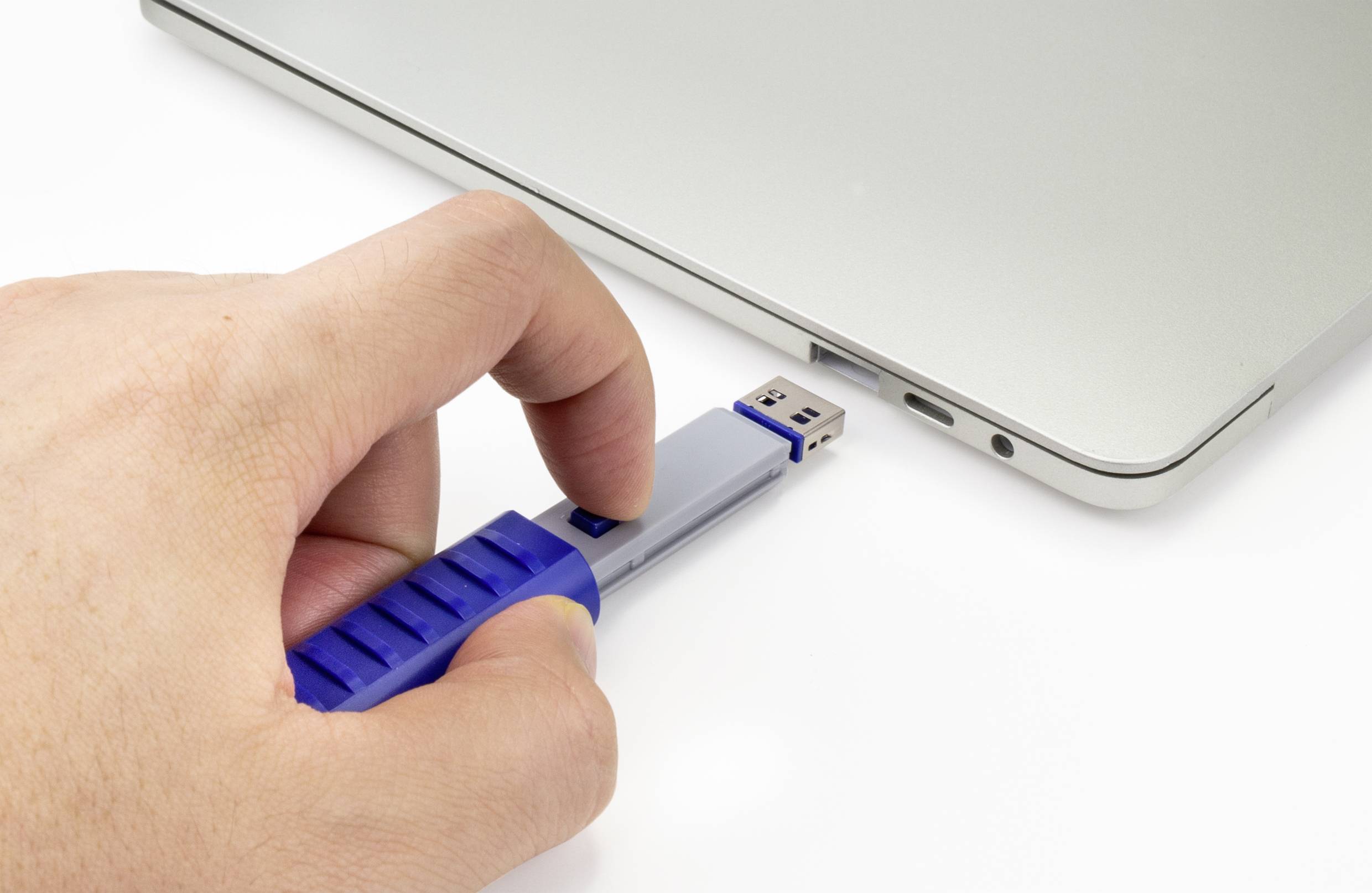 Ręka wkłada niebieski pendrive do laptopa.