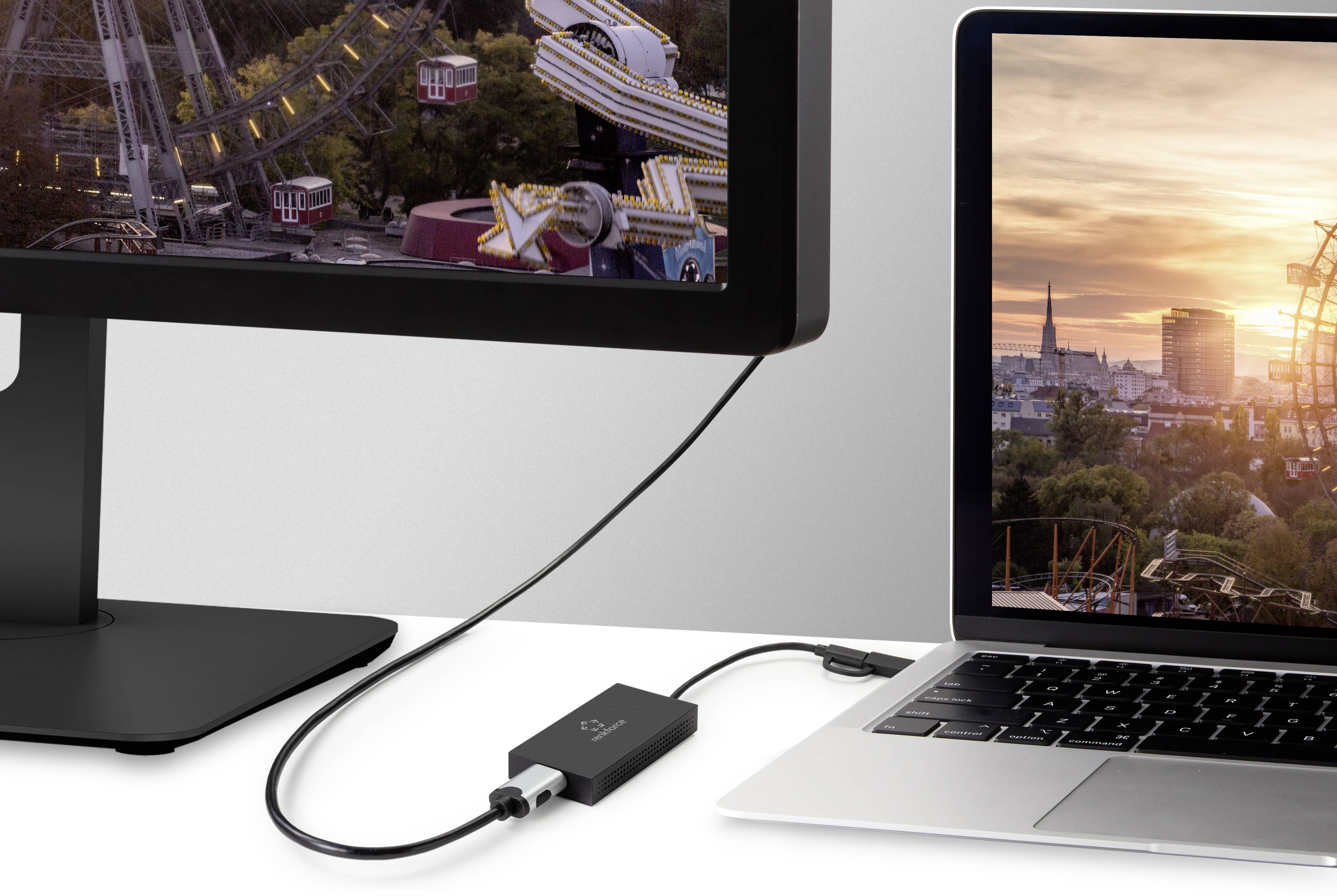 Laptop jest połączony z monitorem. Pomiędzy nimi umieszczony jest adapter. Monitor wyświetla obraz diabelskiego młyna o zachodzie słońca.