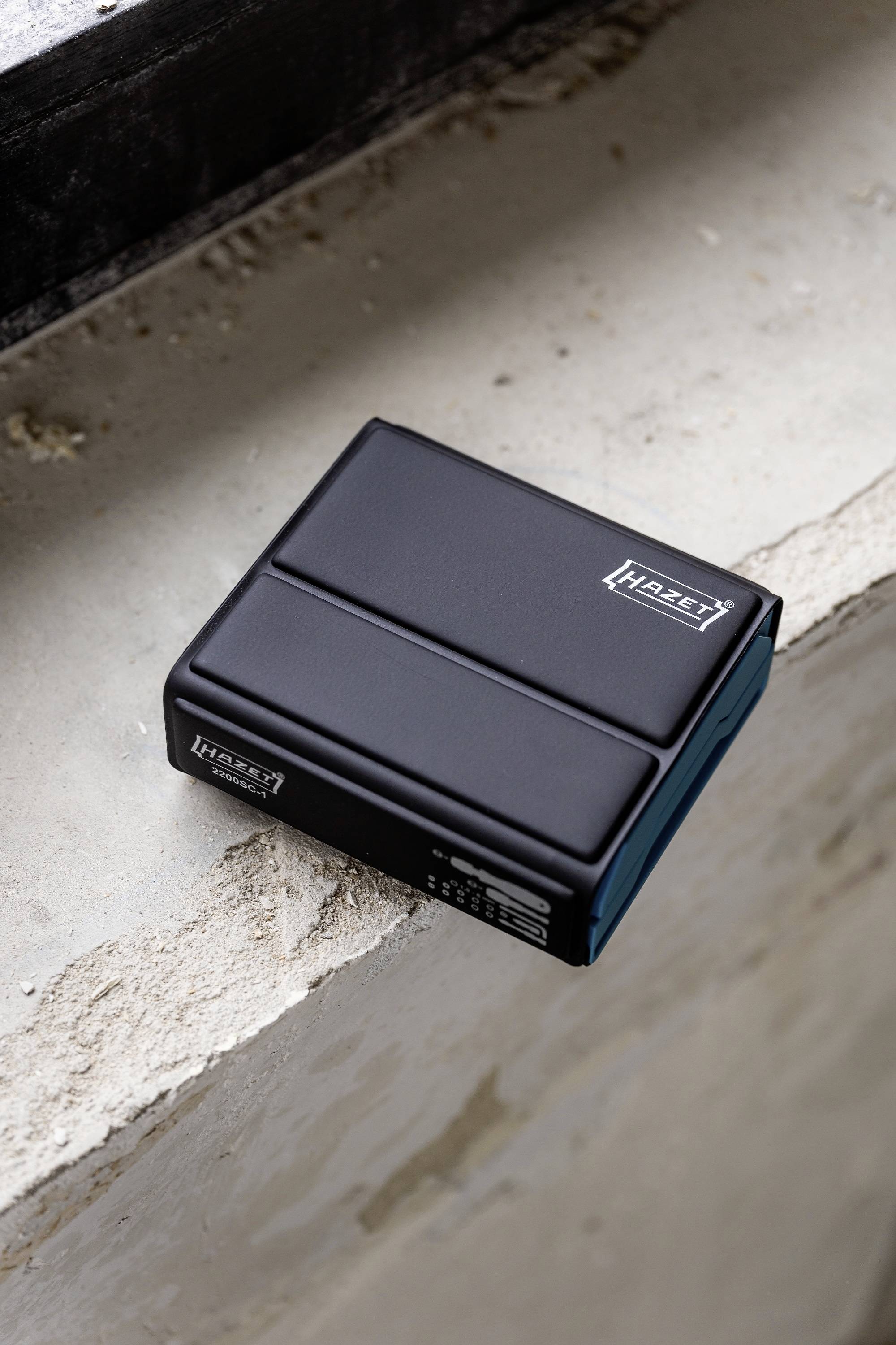 Na betonowym parapecie leży czarna stacja ładowania z logo marki na wierzchu.