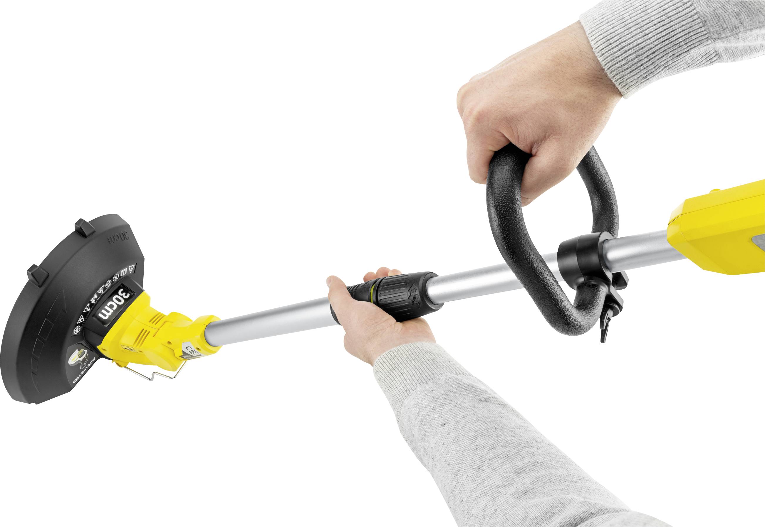 Osoba trzyma żółty trymer do trawy obiema rękami. Urządzenie posiada czarną osłonę ochronną i ergonomiczny uchwyt.