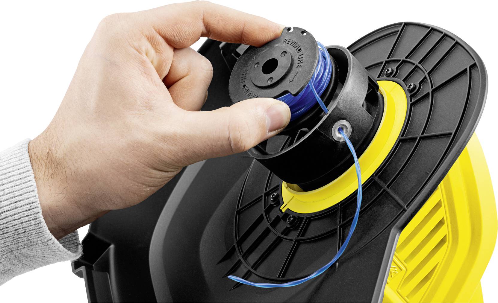 Mężczyzna wymienia żyłkę w kosiarce spalinowej. Jego ręka trzyma szpulę, podczas gdy niebieski sznurek jest wprowadzany przez otwór.