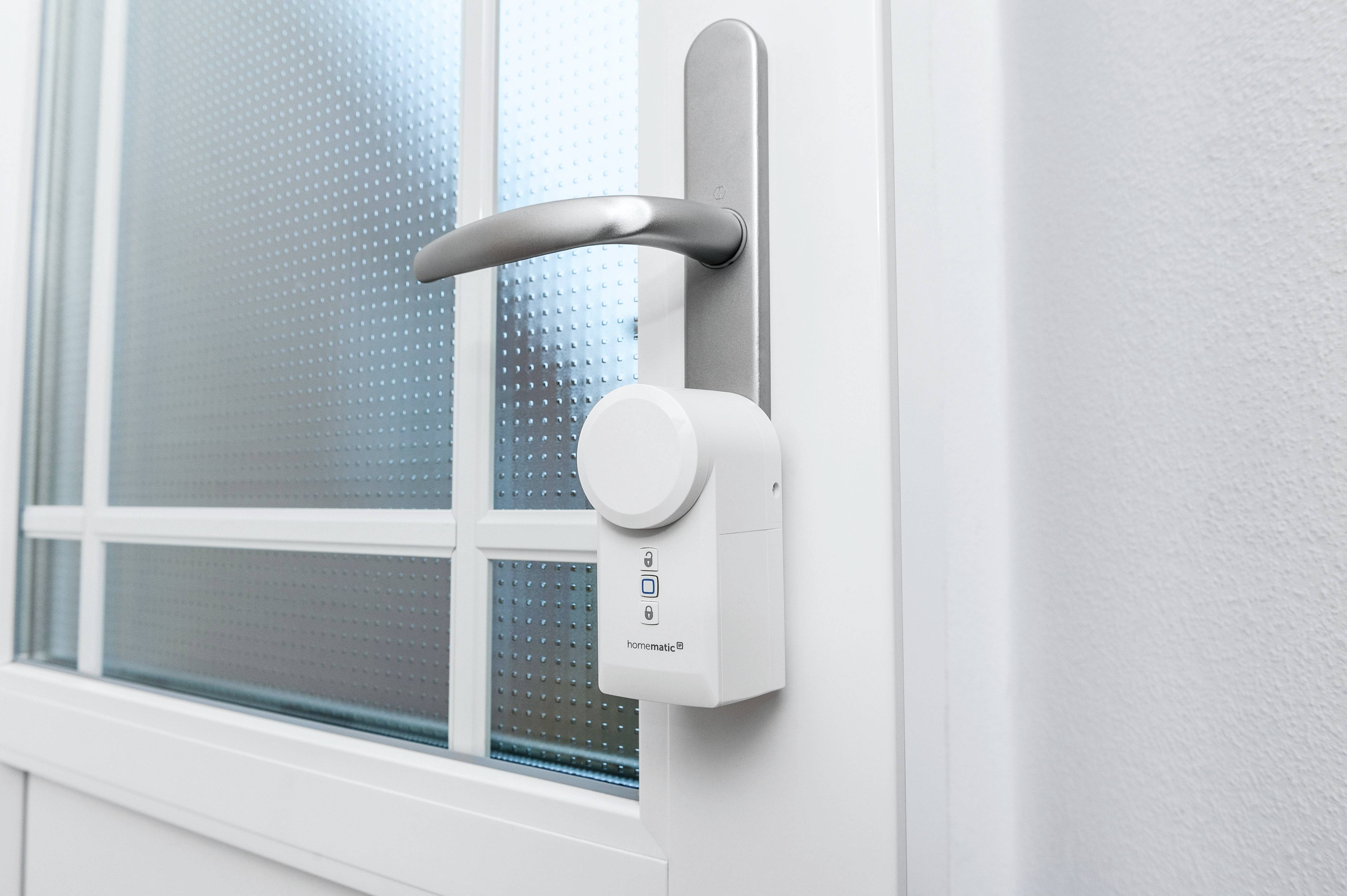 Elektroniczny zamek do drzwi jest wmontowany w białe drzwi z elementami szklanymi. Zamek posiada klawiaturę oraz logo 'homematic IP'.