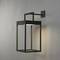 Nowoczesna lampa naścienna o prostokątnym kształcie z czarną ramą, zamontowana na szarej ścianie, oświetla obszar poniżej niej.