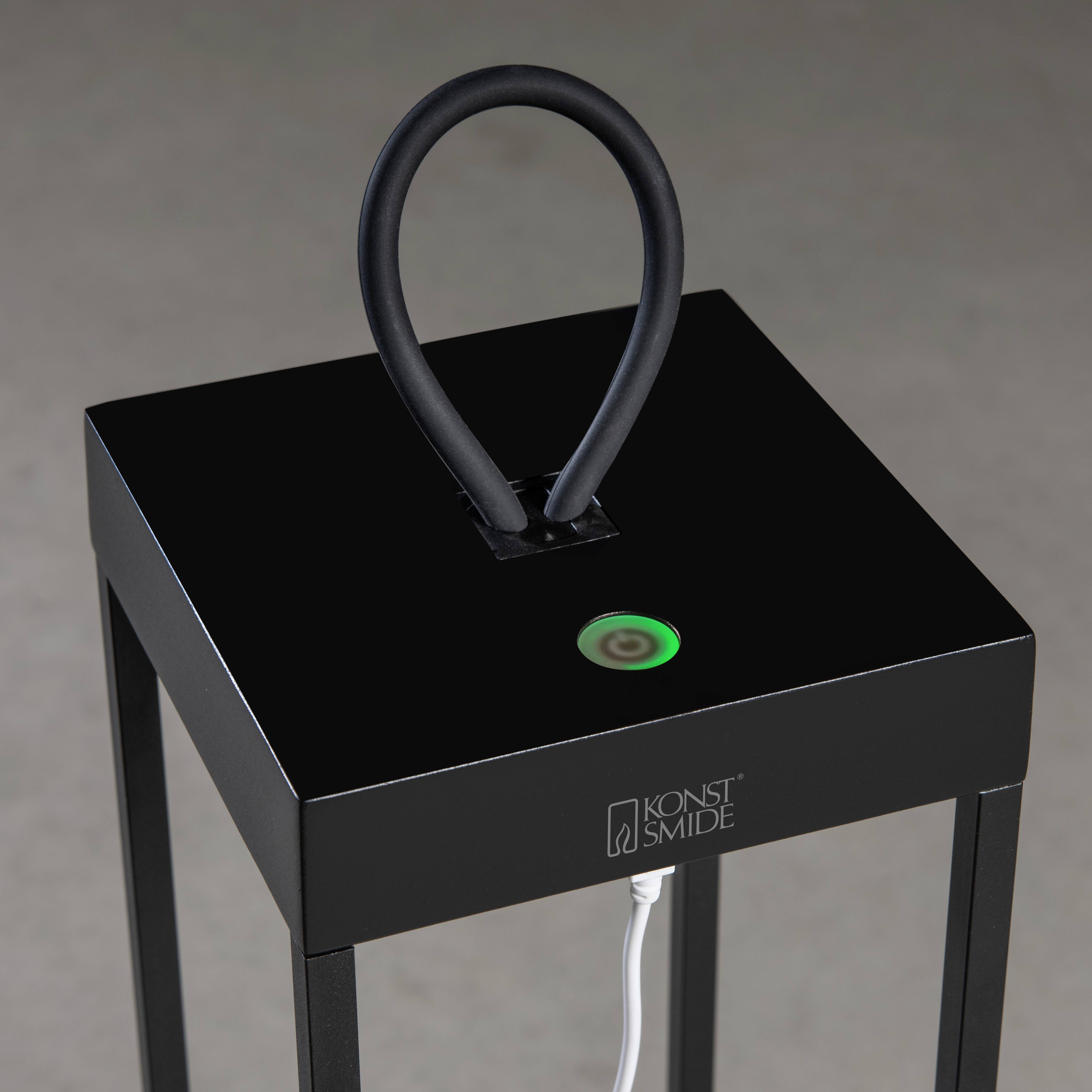 Czarna lampa stołowa z prostokątną podstawą i zakrzywionym uchwytem. Widoczny jest zielony przycisk z przewodem.
