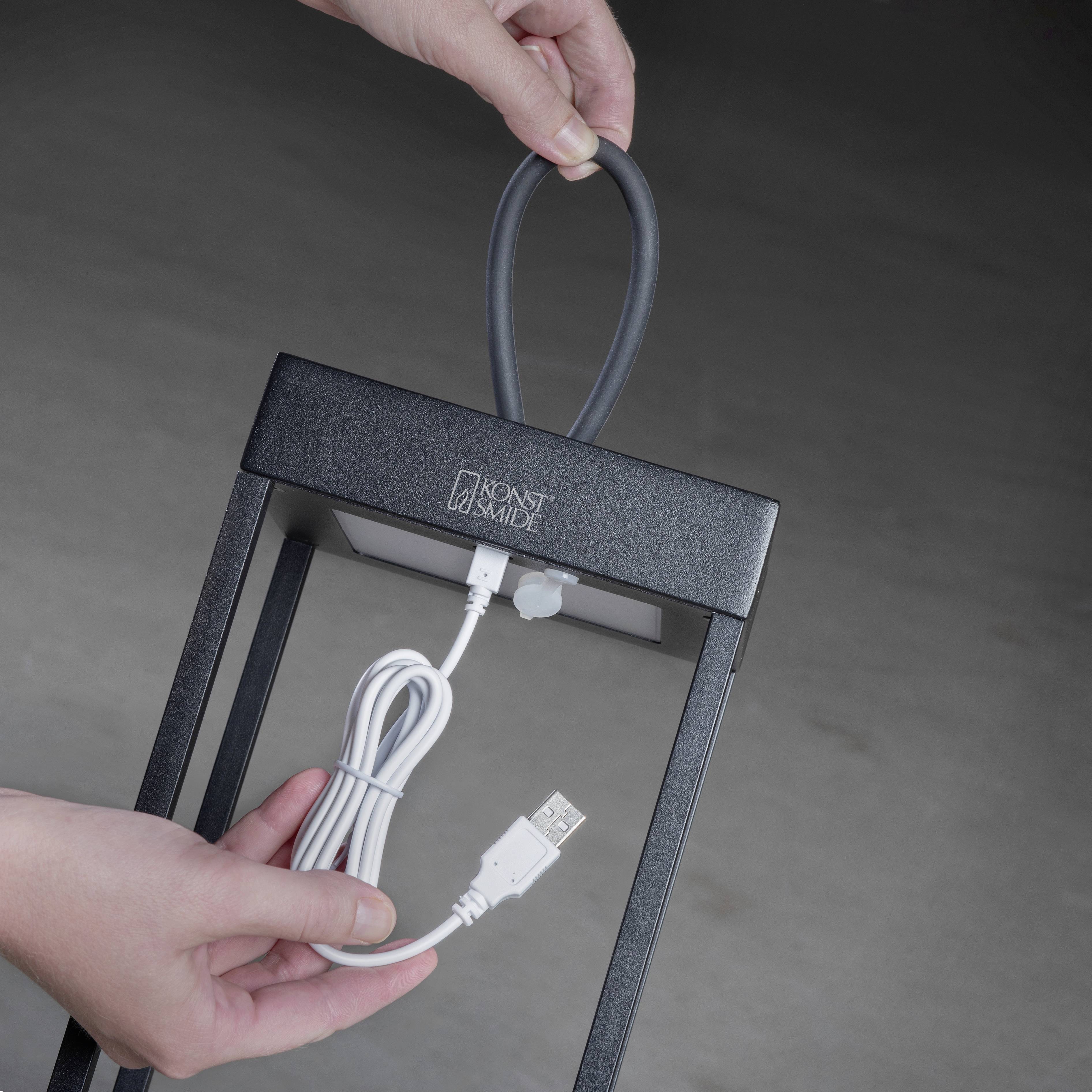 Osoba trzyma przenośną latarkę z przewodem USB w ręku. Latarka ma nowoczesny design i jest czarna.