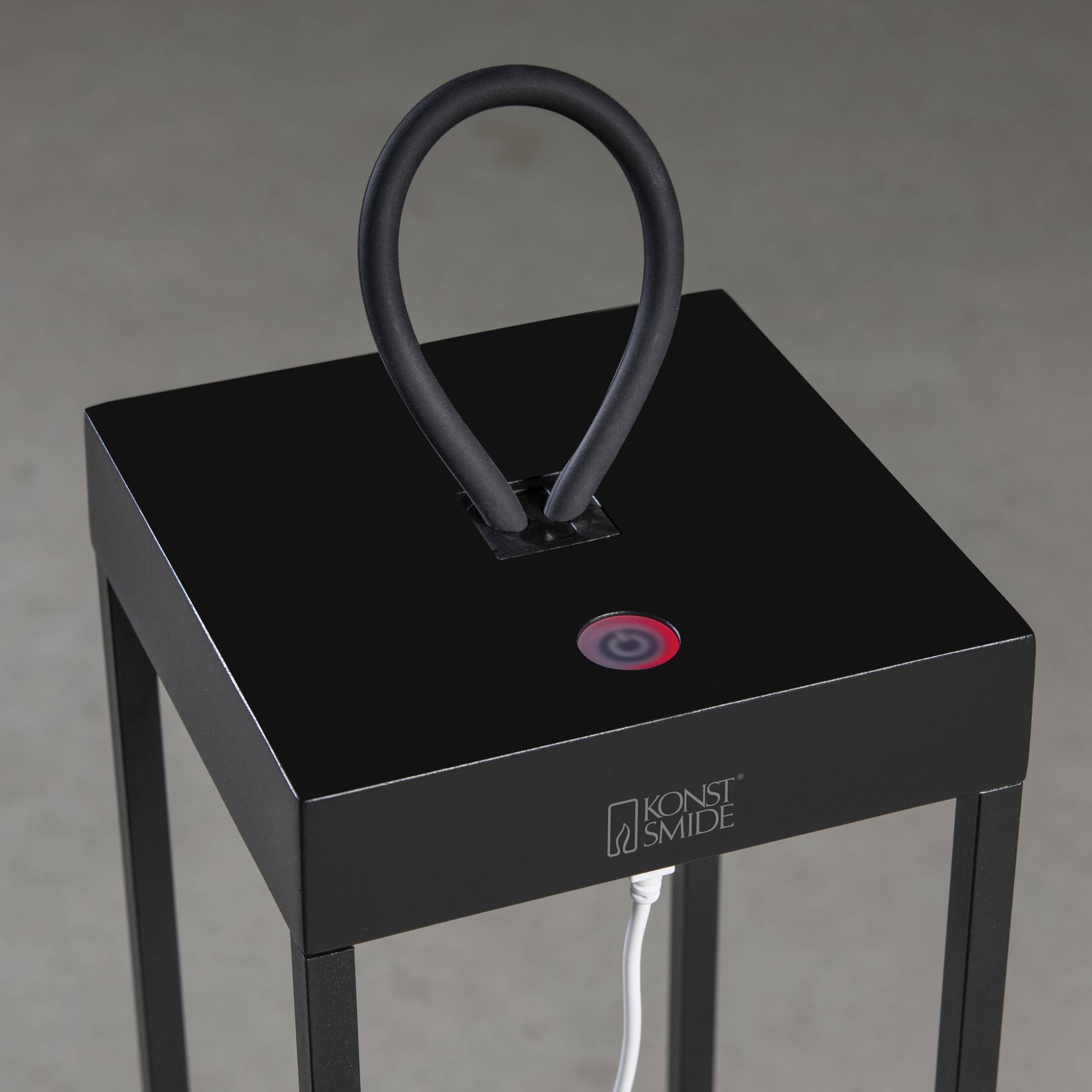 Czarna lampa stołowa z kwadratową podstawą, czerwonym włącznikiem i giętym ramieniem. Widoczna jest marka 'Konst Smide'.
