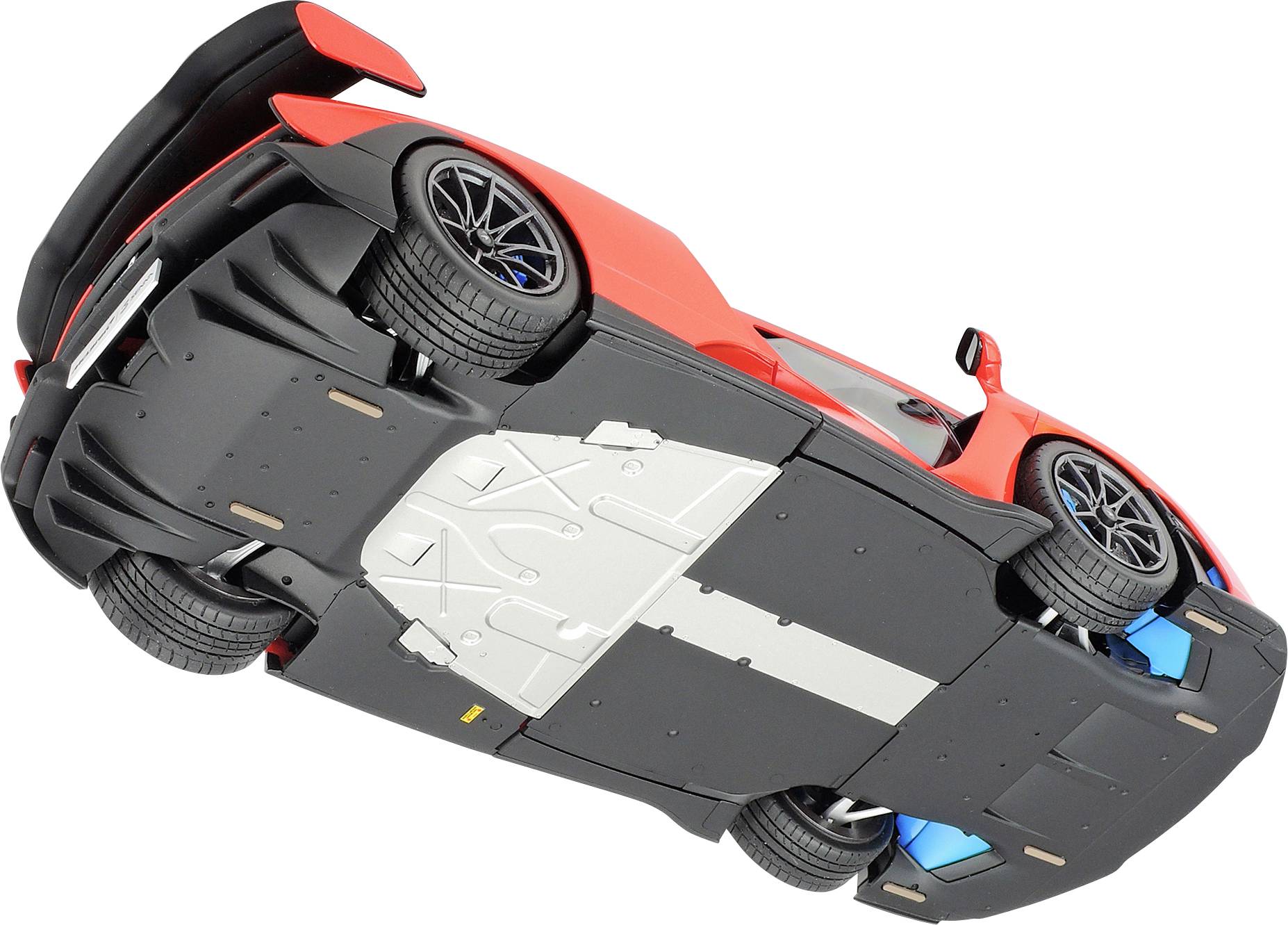 Czerwony samochód sportowy sfotografowany od dołu, z widocznym podwoziem i bieżnikiem opon, na białym tle.