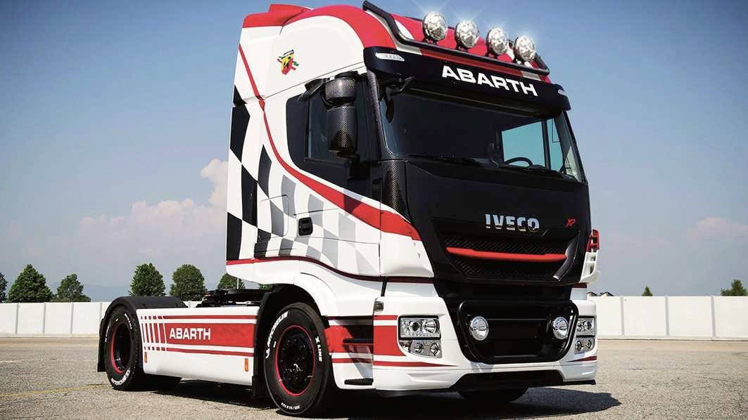 Czerwono-biało-czarna ciężarówka Iveco z logo Abarth stoi na parkingu. Pojazd wyróżnia się efektownym wzorem rajdowych pasów.