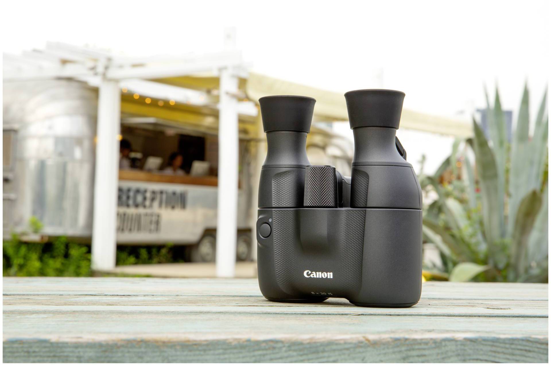 Obraz przedstawia lornetkę na drewnianym stole na świeżym powietrzu. W tle widoczny jest srebrny znacznik z napisem 'Reception Counter'.