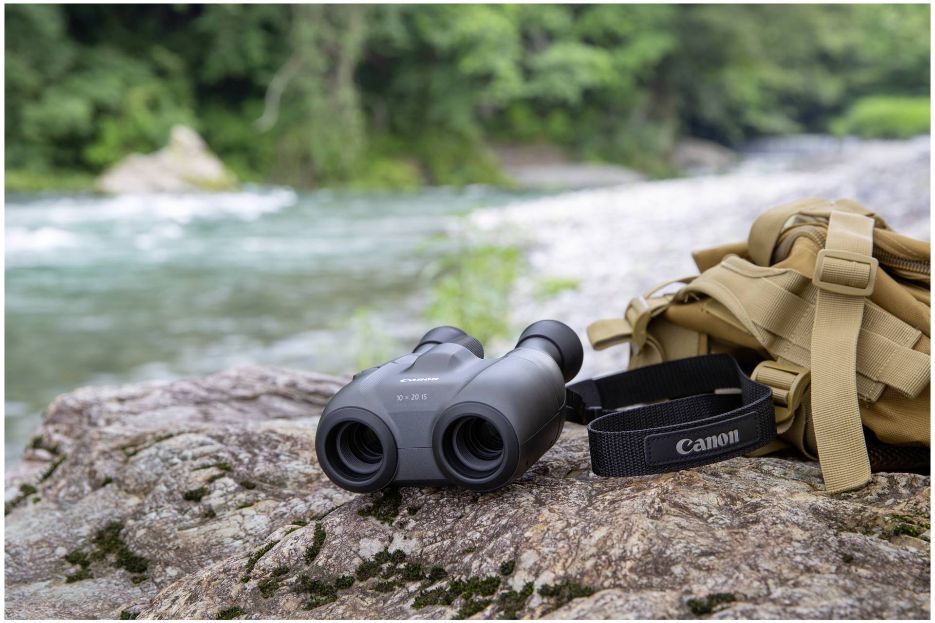 Lornetka i plecak leżą na kamieniu nad brzegiem rzeki. Rzeka płynie przez zieloną krajobrazową dolinę w tle.