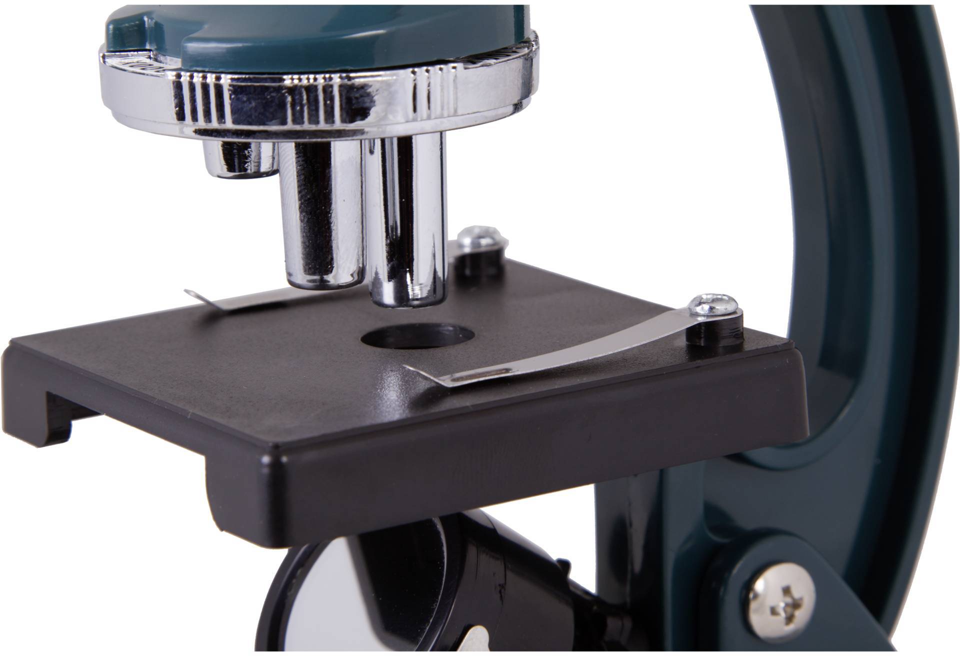 Zbliżenie mikroskopu z czarnym uchwytem na preparat i srebrnymi zaciskami. Widoczny system soczewek i części podstawy.