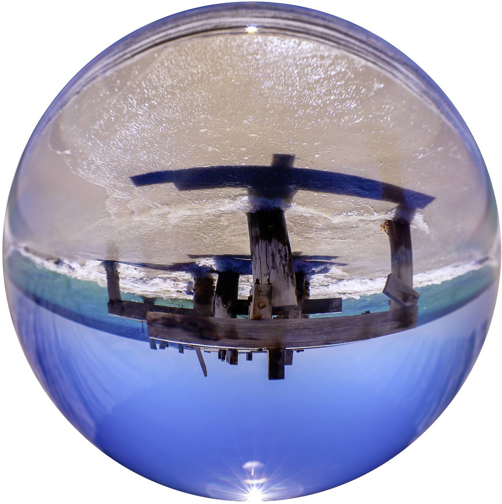 Stara, drewniana marina stoi na plaży, otoczona błękitnym niebem i pianistymi falami, sfotografowana w perspektywie rybie.