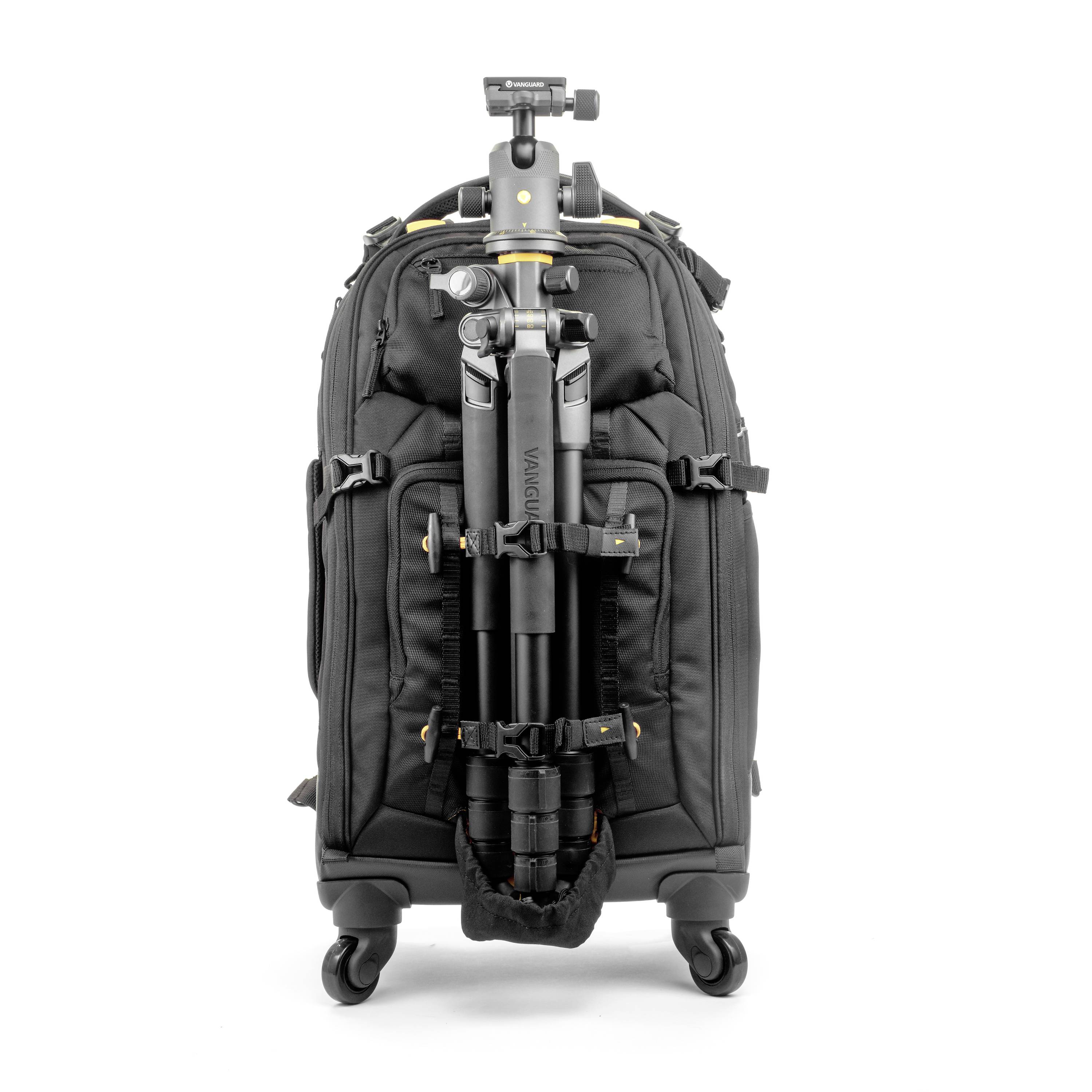 Średniej wielkości czarny plecak podróżny na sprzęt fotograficzny z zamontowanym statywem z przodu, stojący na czterech kółkach.