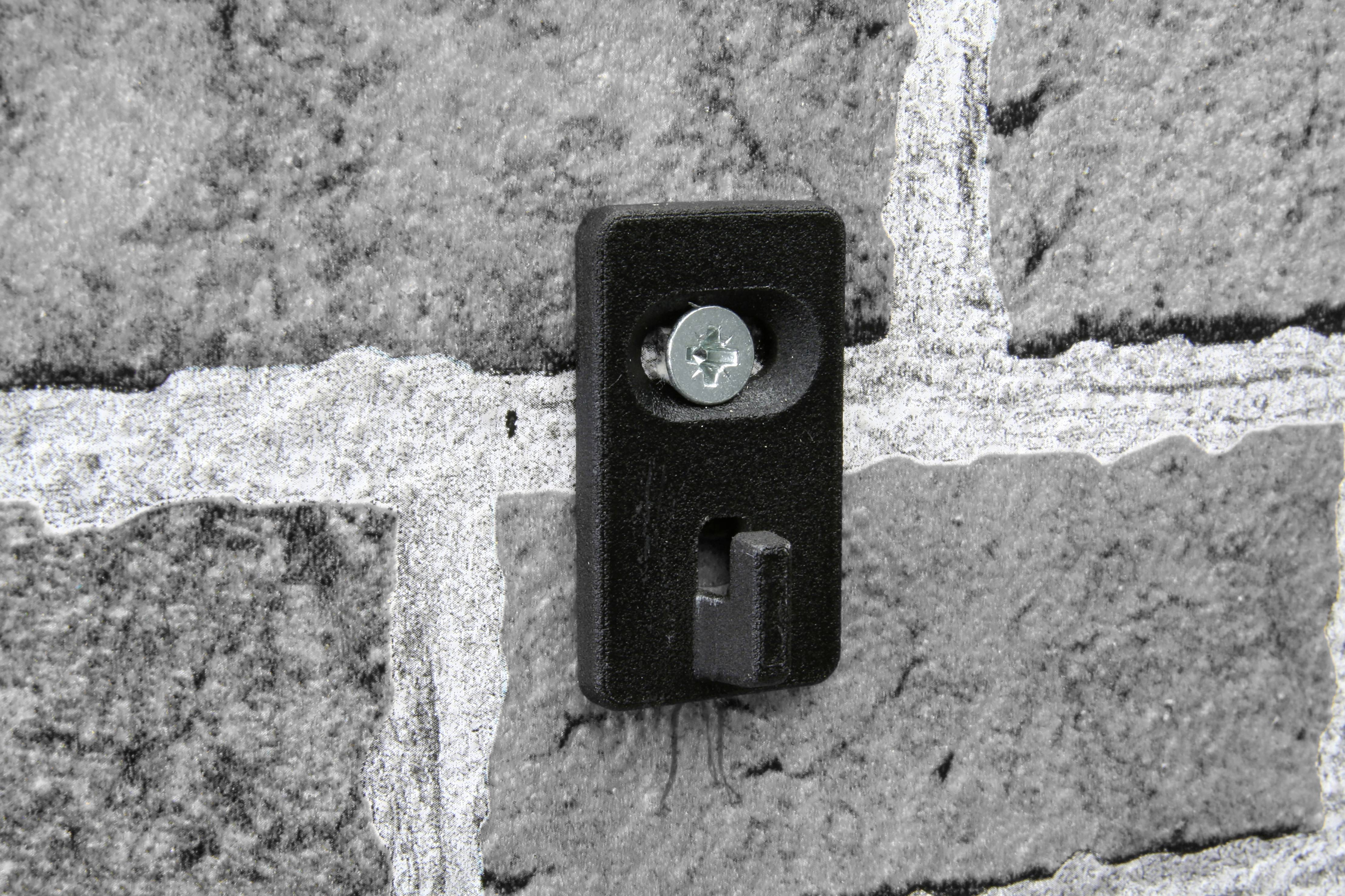 Czarny hak ścienny zamocowany na szarej ścianie z cegły.