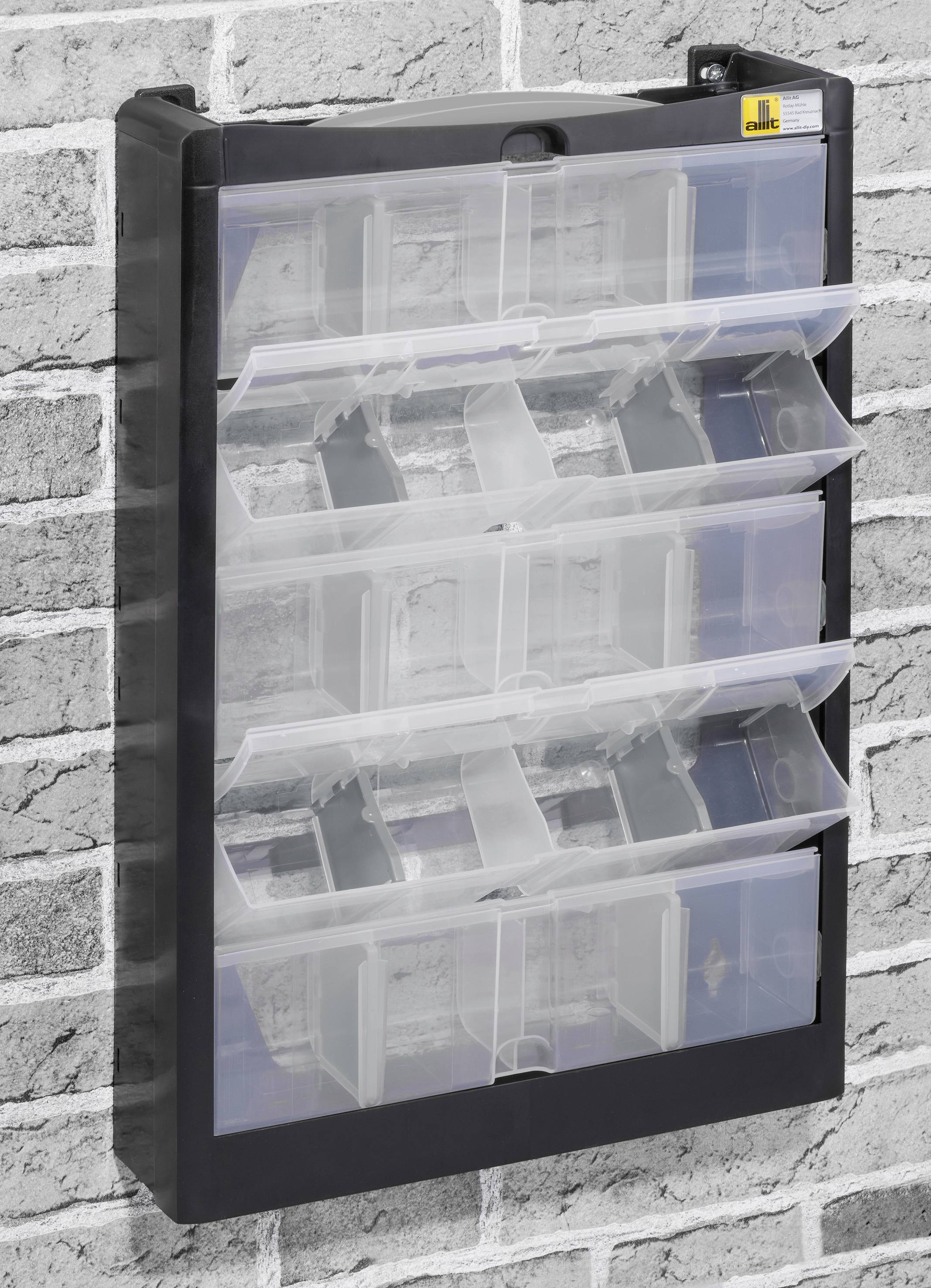 Czarna, mocowana na ścianie półka z tworzywa sztucznego z przezroczystymi klapowanymi przegródkami. Stoi przed szarą murowaną ścianą. Idealna do przechowywania.